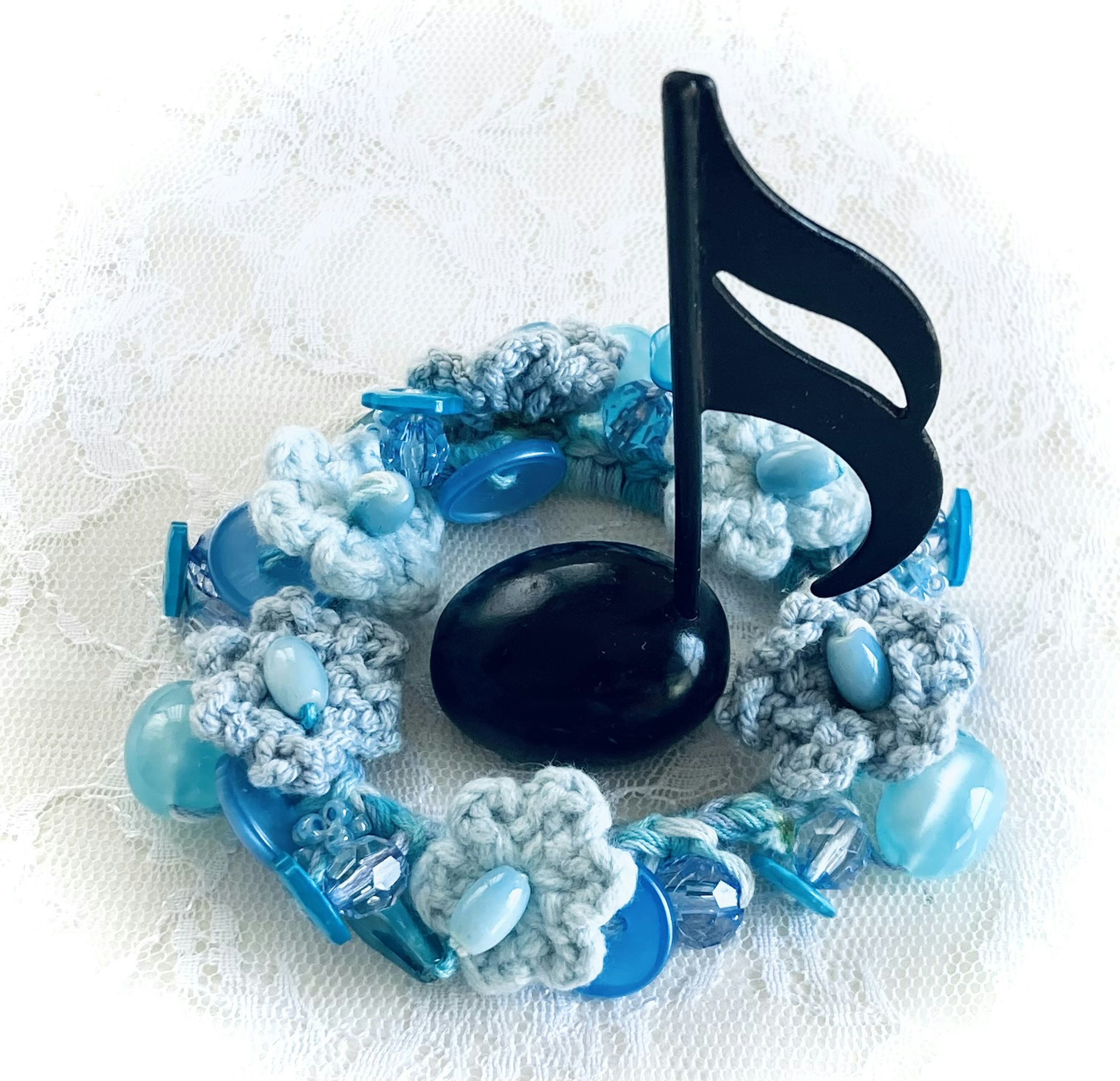 A decorative piece featuring blue flowers and beads with a black musical note standing in the center