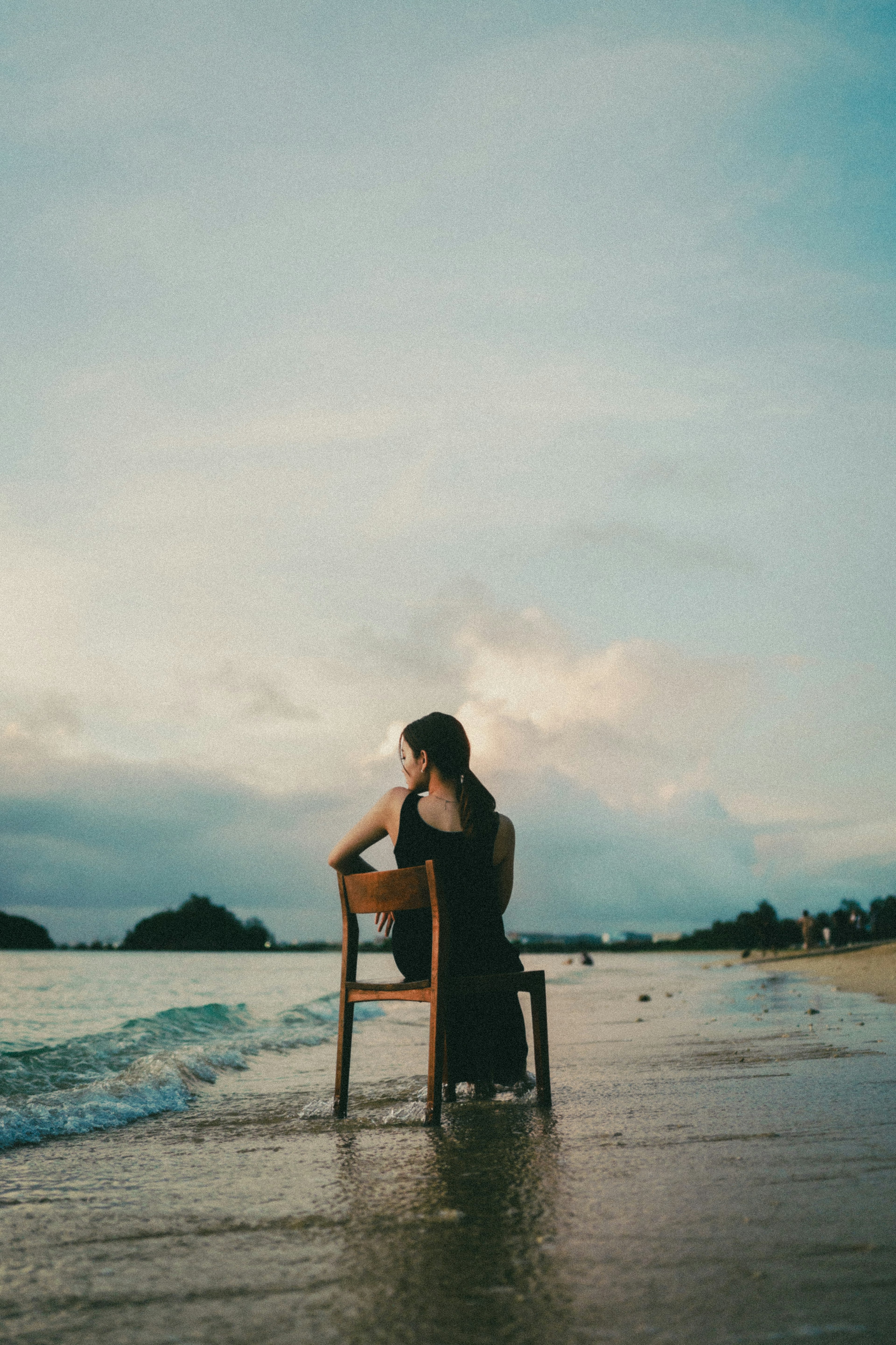 Eine Frau sitzt auf einem Stuhl am Strand mit Ozean und Himmel im Hintergrund