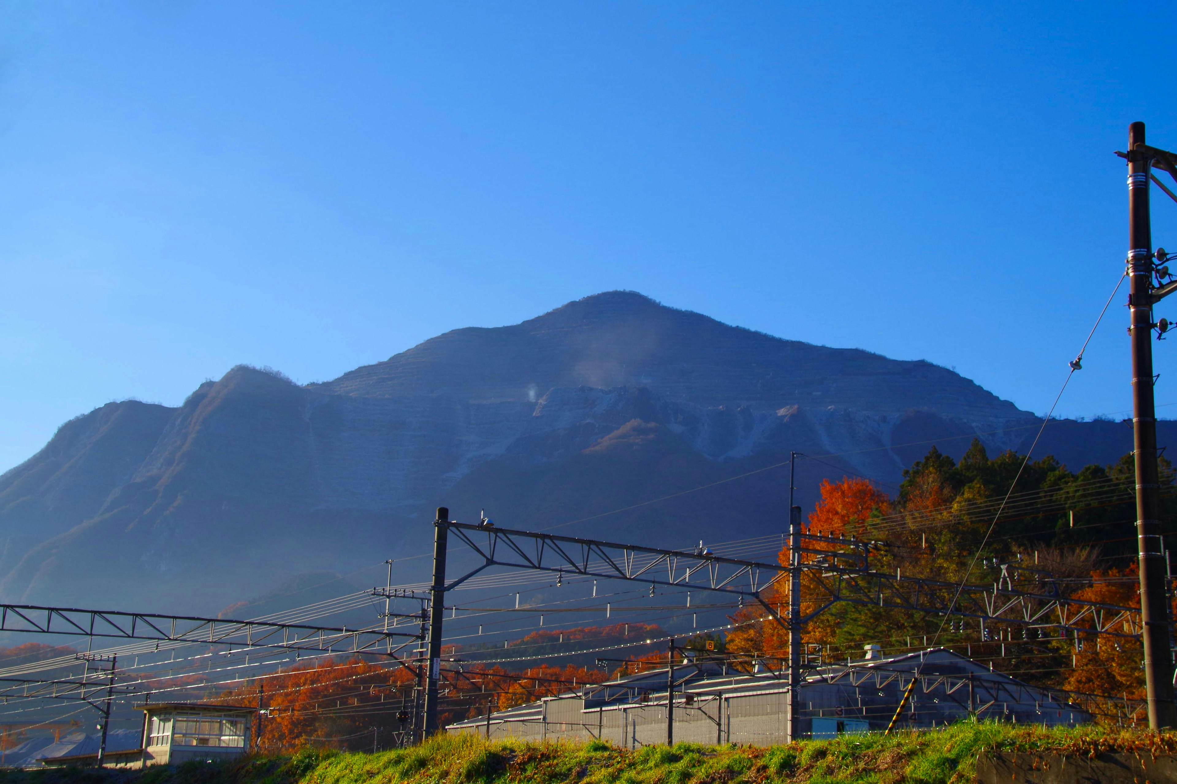 Pemandangan gunung musim gugur dan langit biru dengan rel kereta dan tiang utilitas