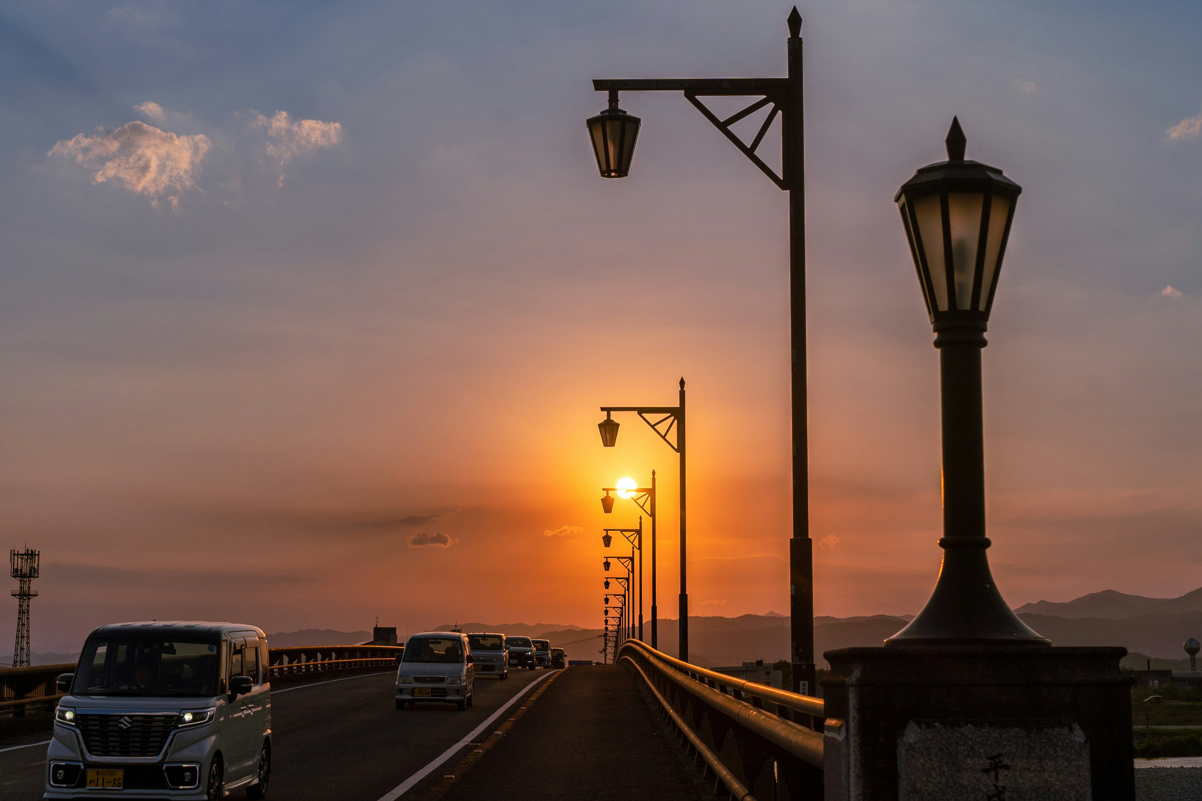 夕日が沈む橋の風景 車が通る道と街灯