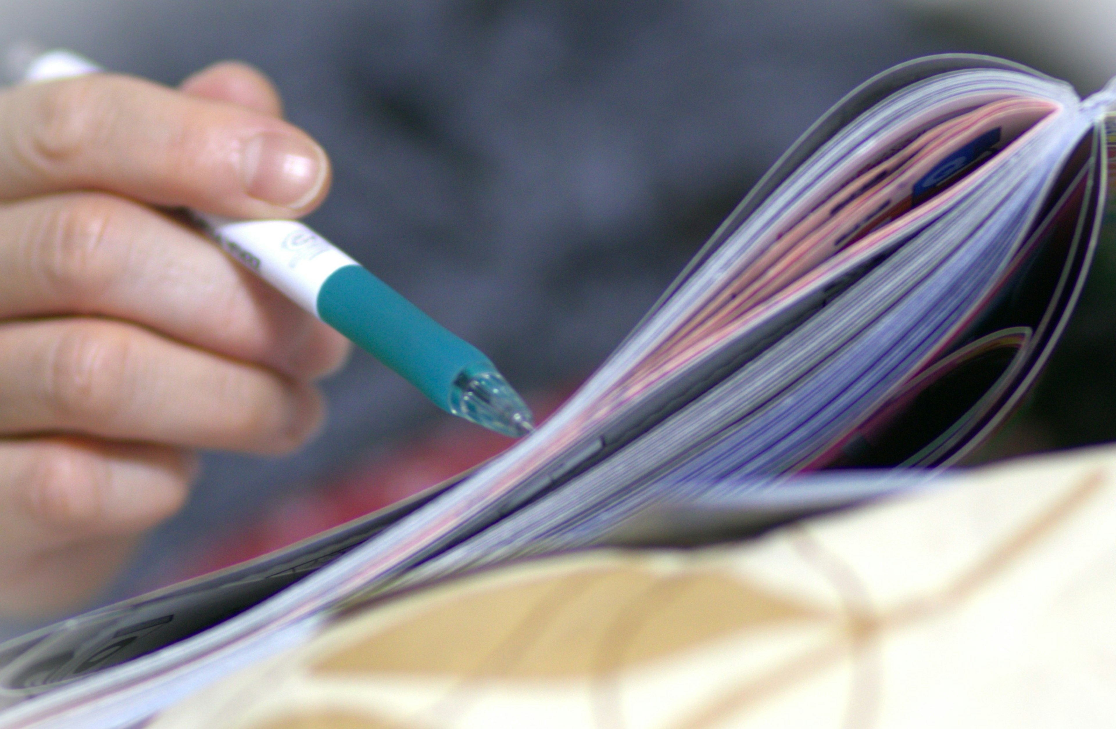 A person holding a blue pen flipping through a magazine