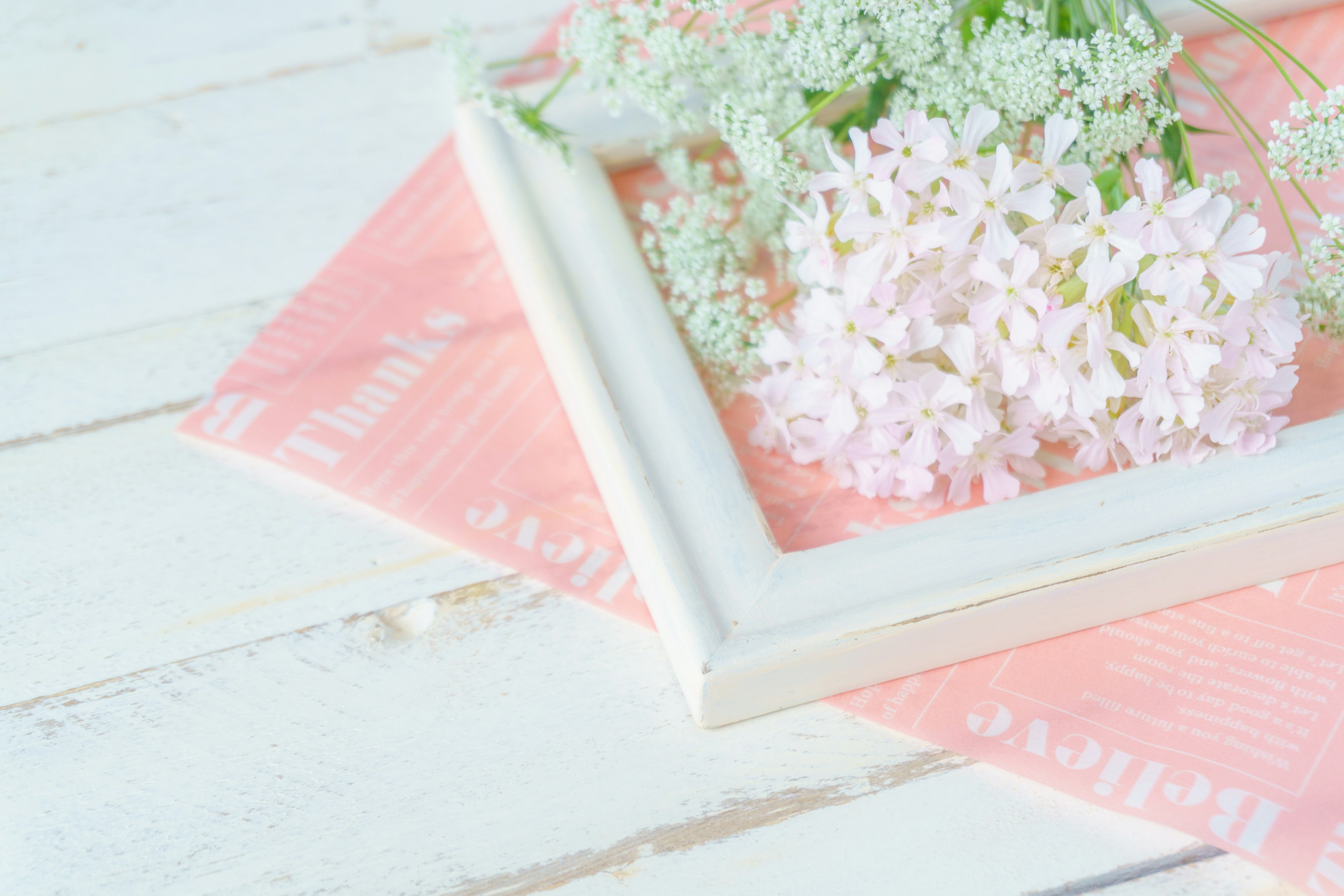 A white frame with pink and white flowers on a soft pastel background