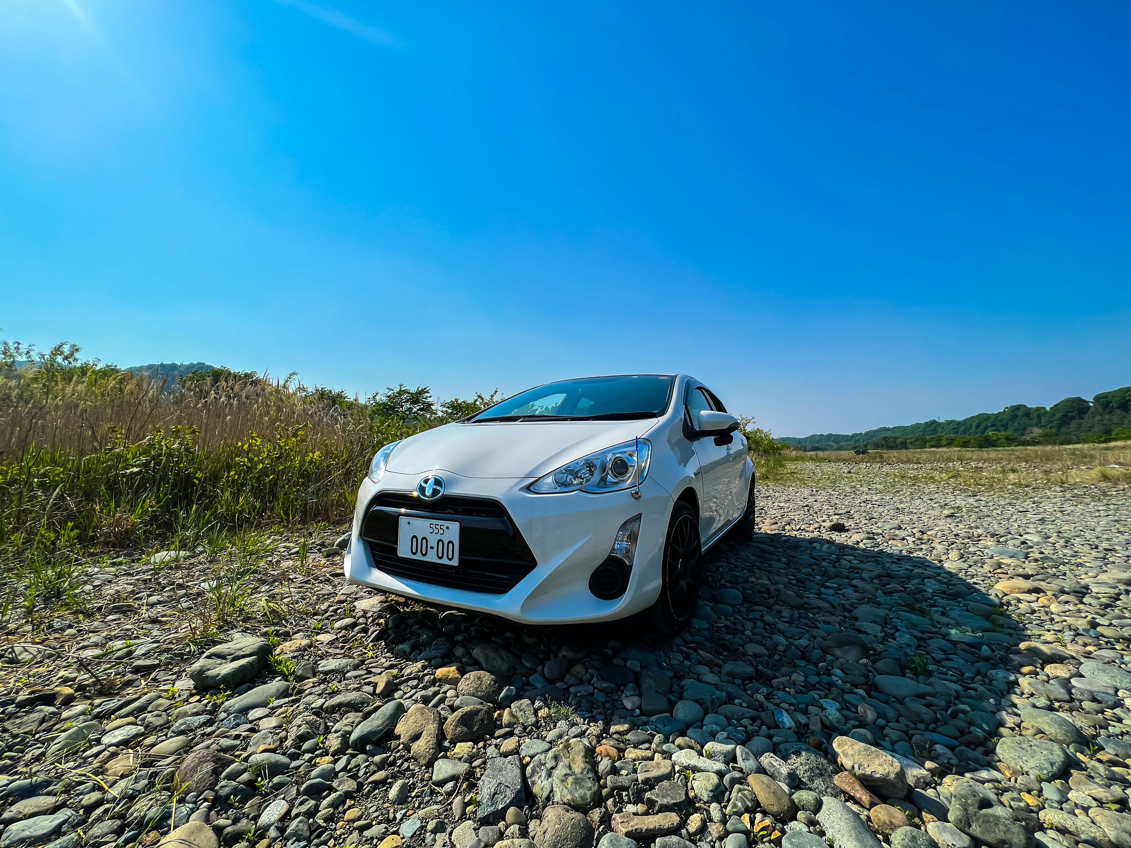 A white Toyota car parked on stones under a blue sky