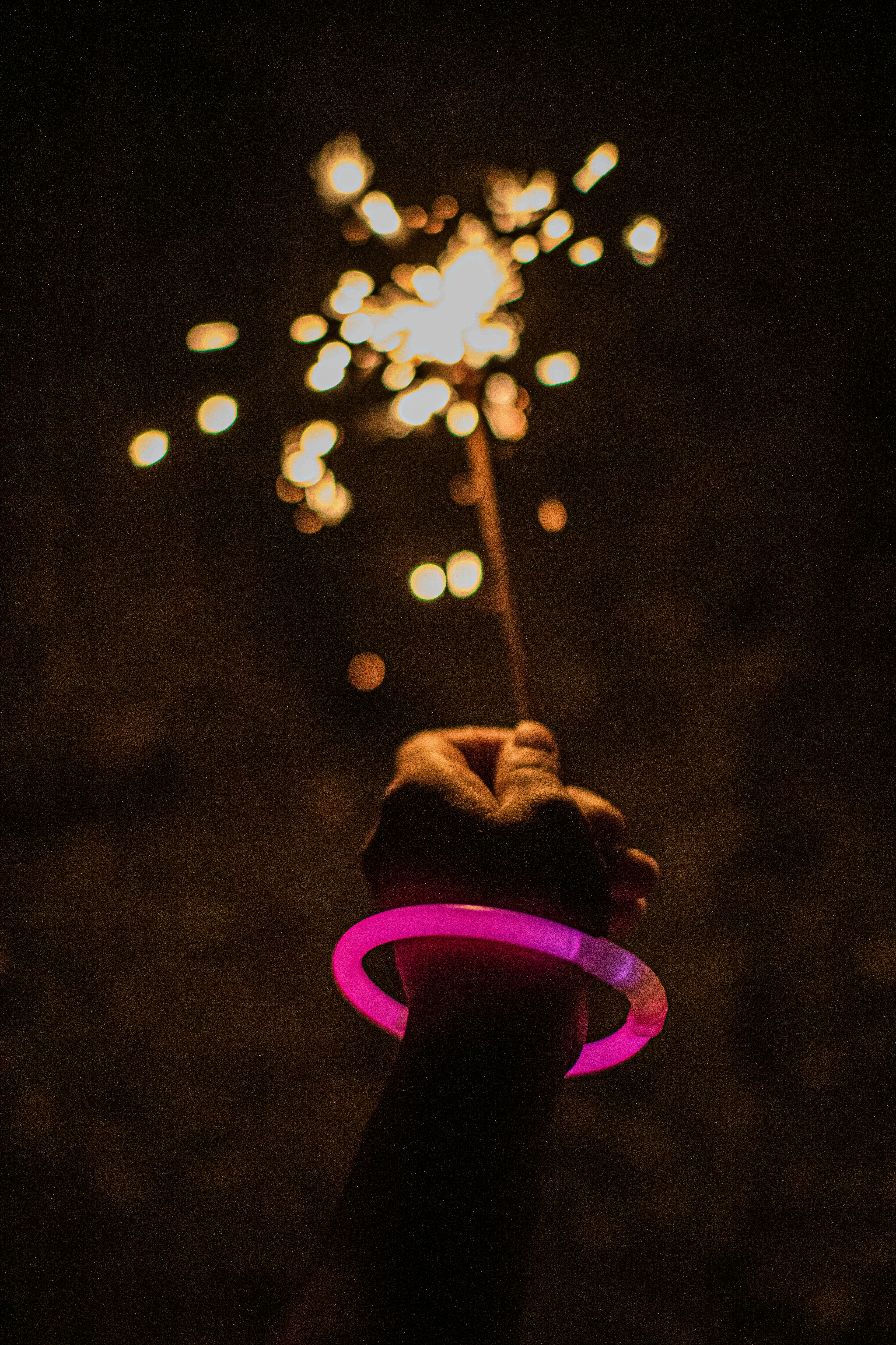 Hand holding a sparkler with a pink glow bracelet