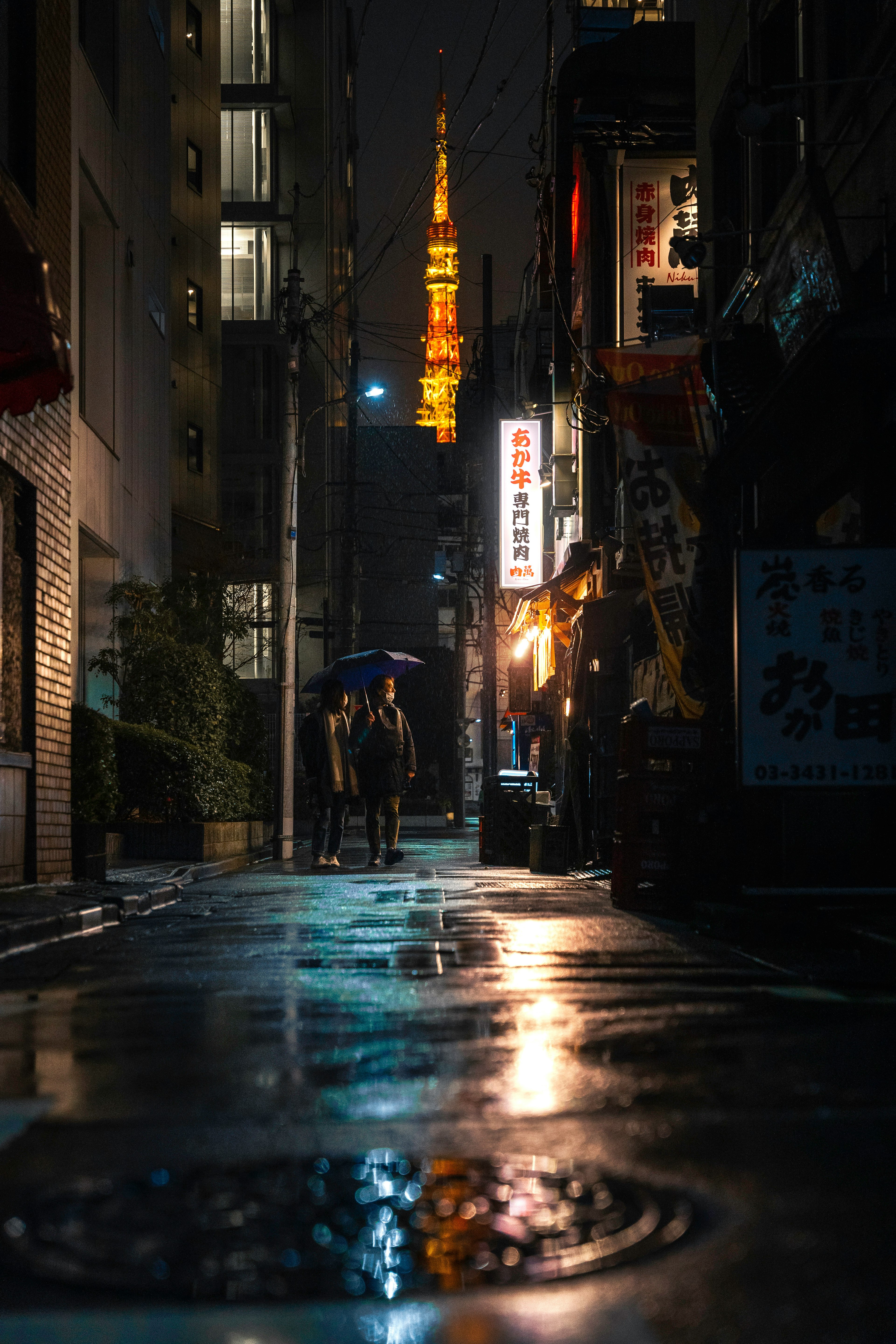 Pasangan berjalan di gang Tokyo di malam hari dengan Menara Tokyo di latar belakang