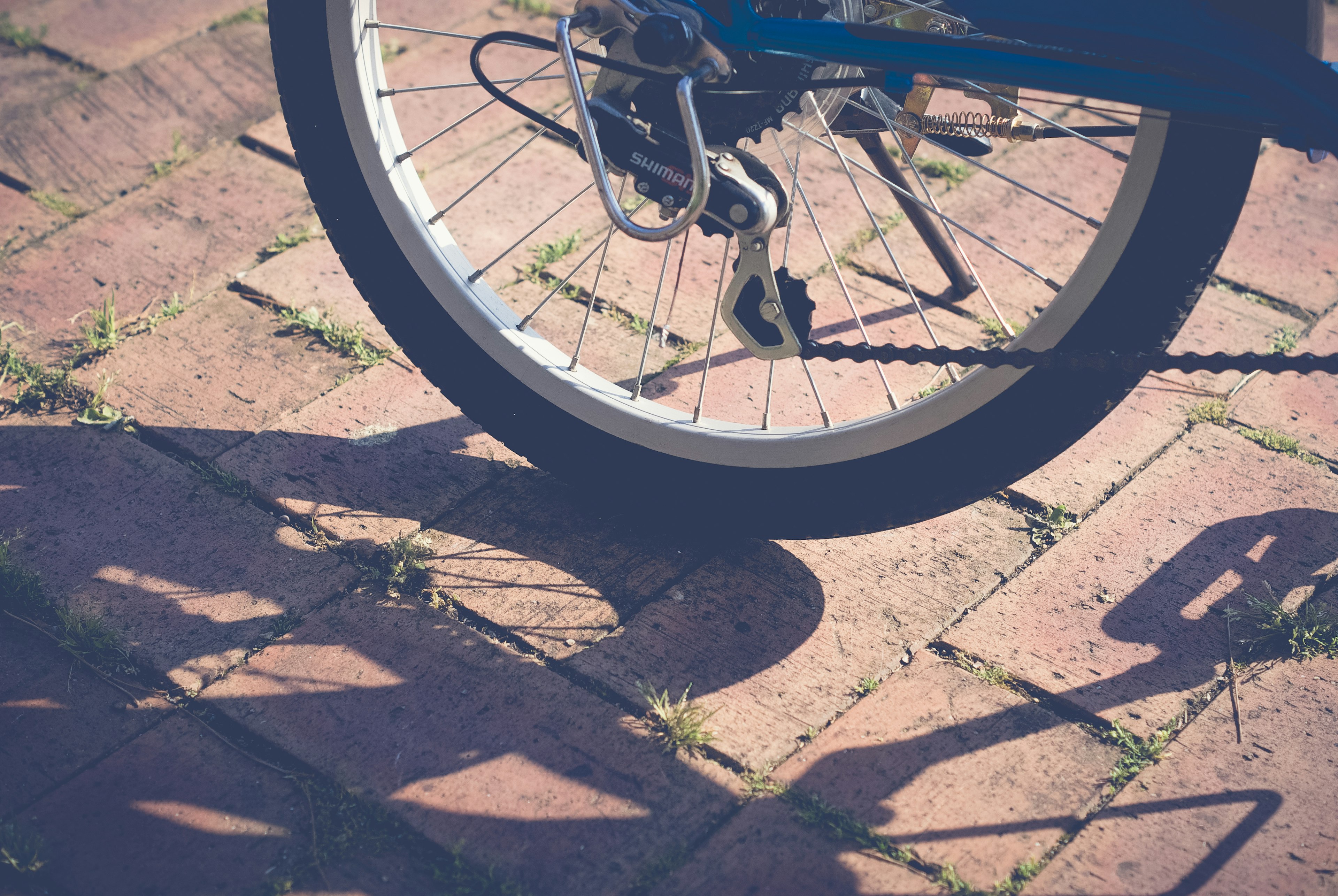 Imagen de una rueda trasera de bicicleta apoyada sobre una superficie de ladrillos con sombras proyectadas