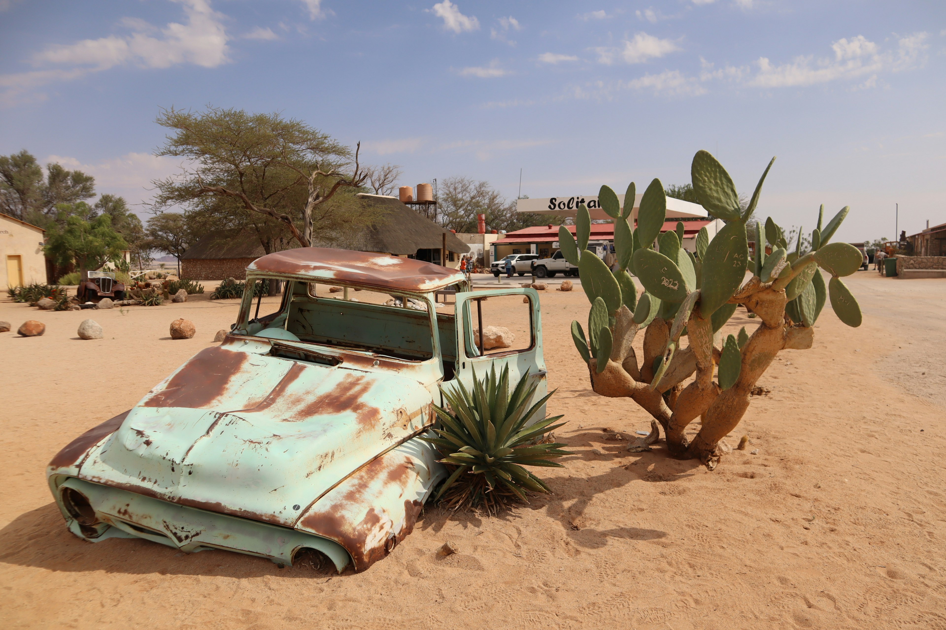 Rusty teal vintage car in a desert landscape with cacti nearby