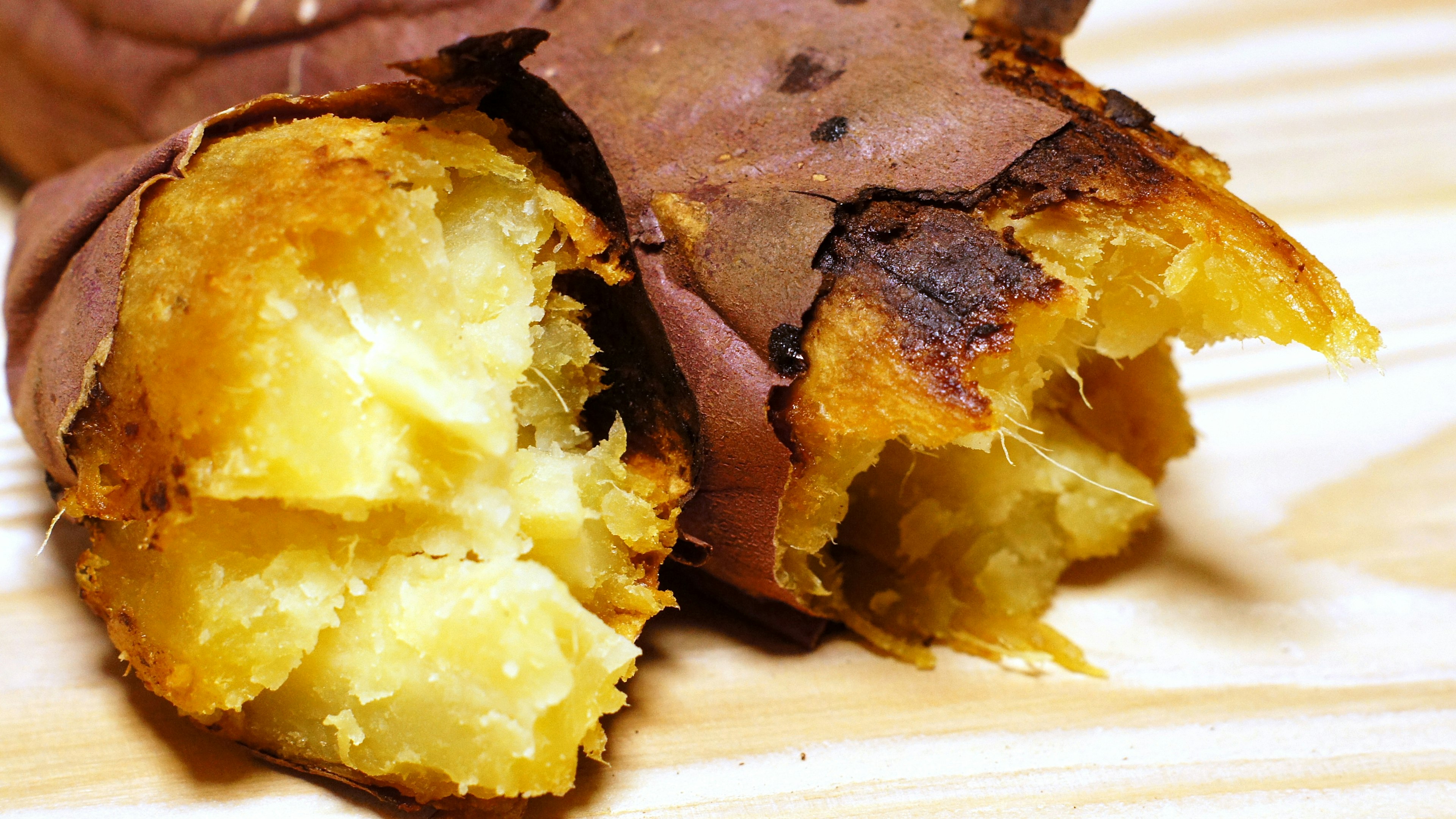 Primer plano de una batata asada parcialmente envuelta en hojas marrones mostrando su interior amarillo suave