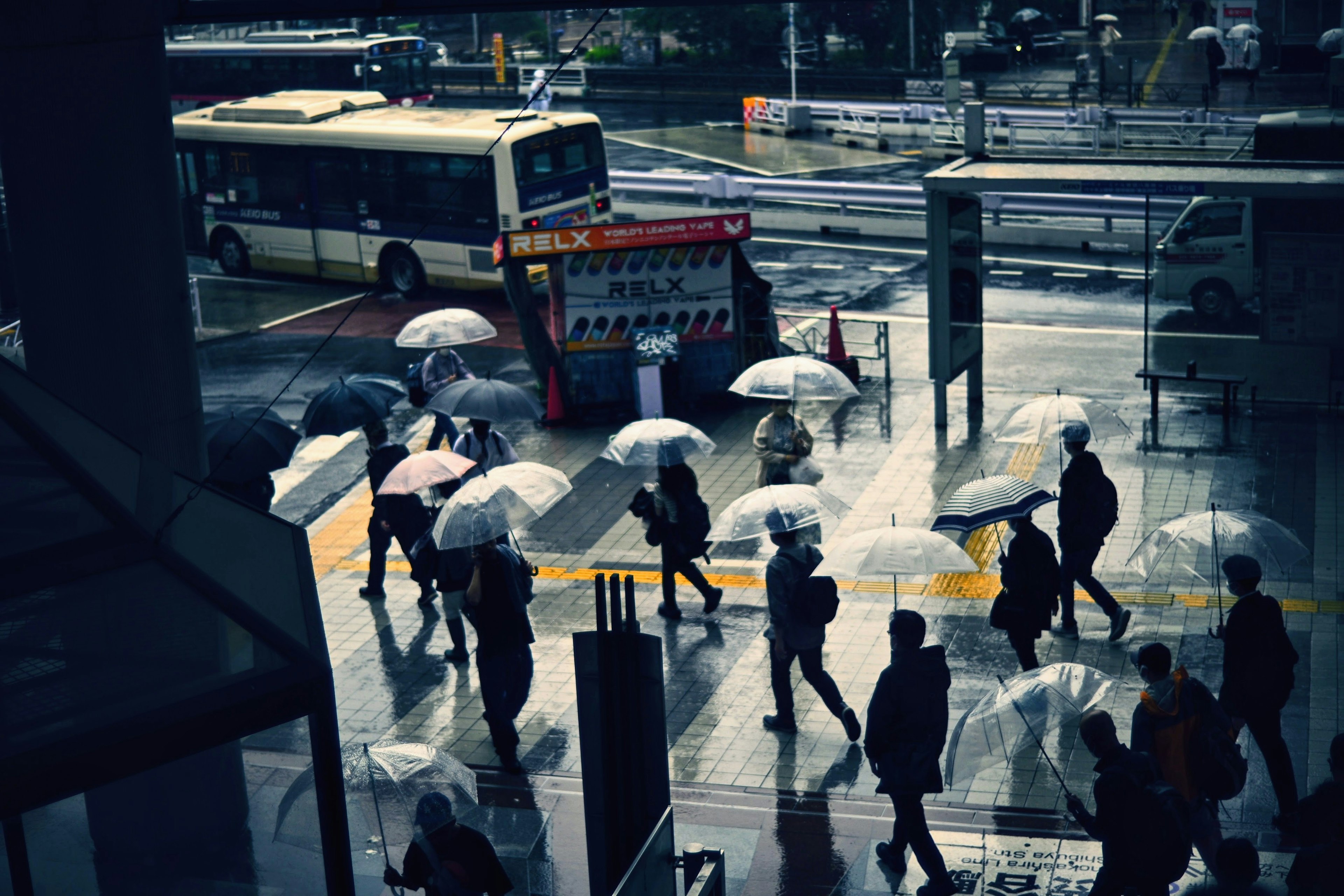 雨の中を歩く人々と傘、バス停の風景