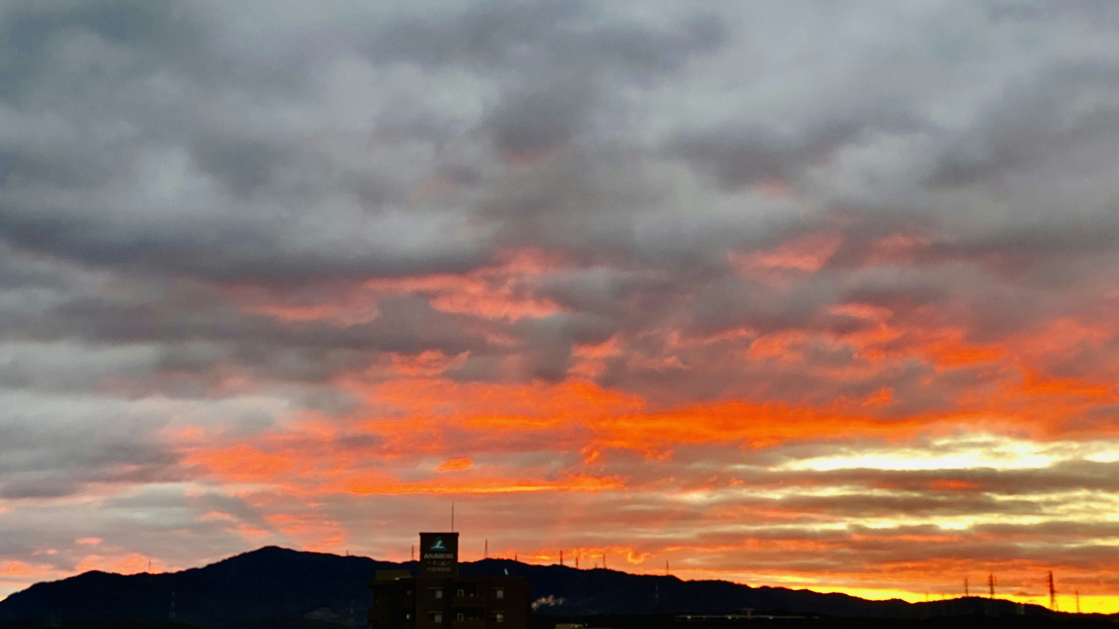 Lebendiger Sonnenuntergangshimmel mit orangefarbenen und grauen Wolken, die einen Berg umreißen