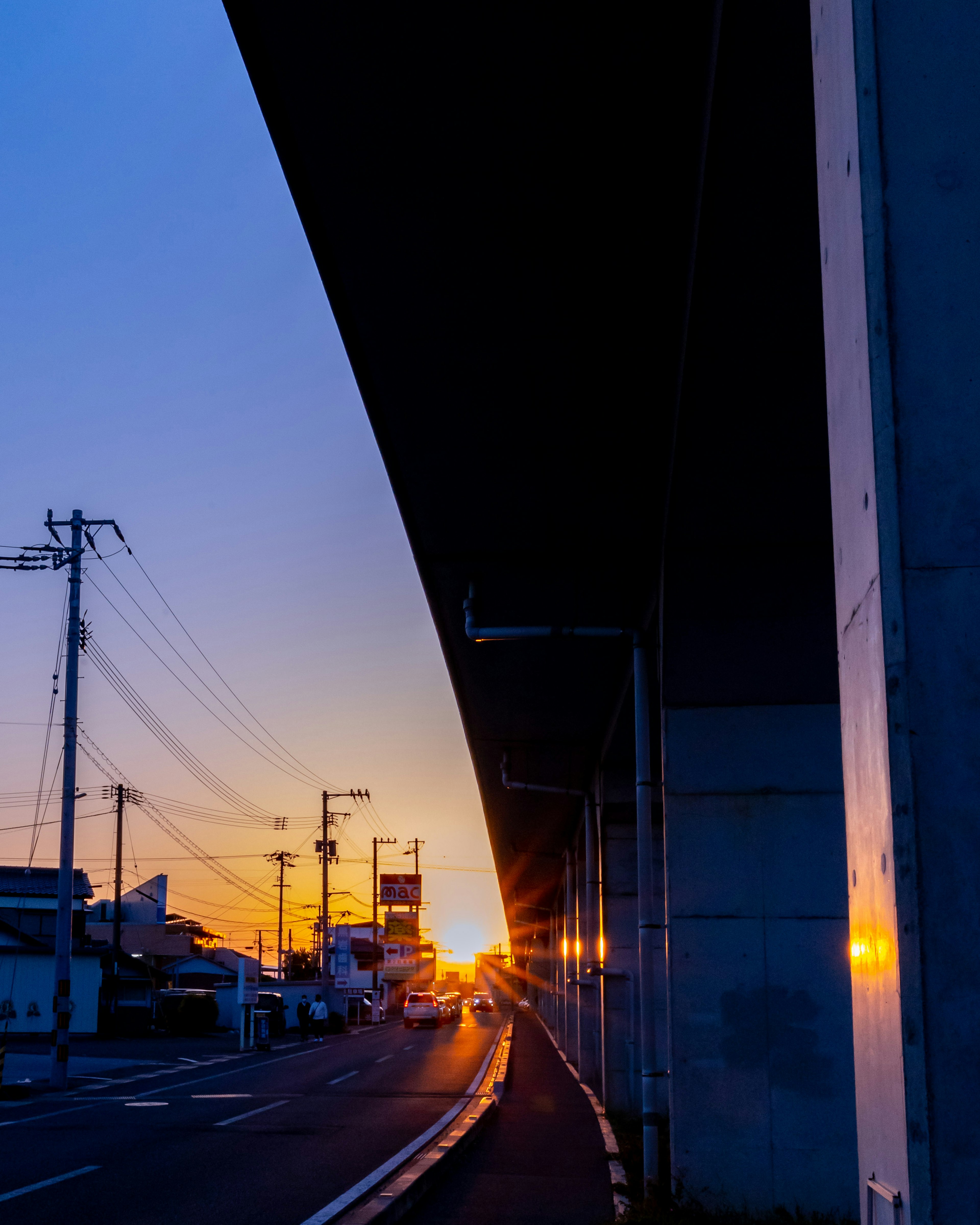 Dämmerungsszene mit einer Straße unter einer erhöhten Struktur Sonnenuntergang reflektiert auf Gebäuden