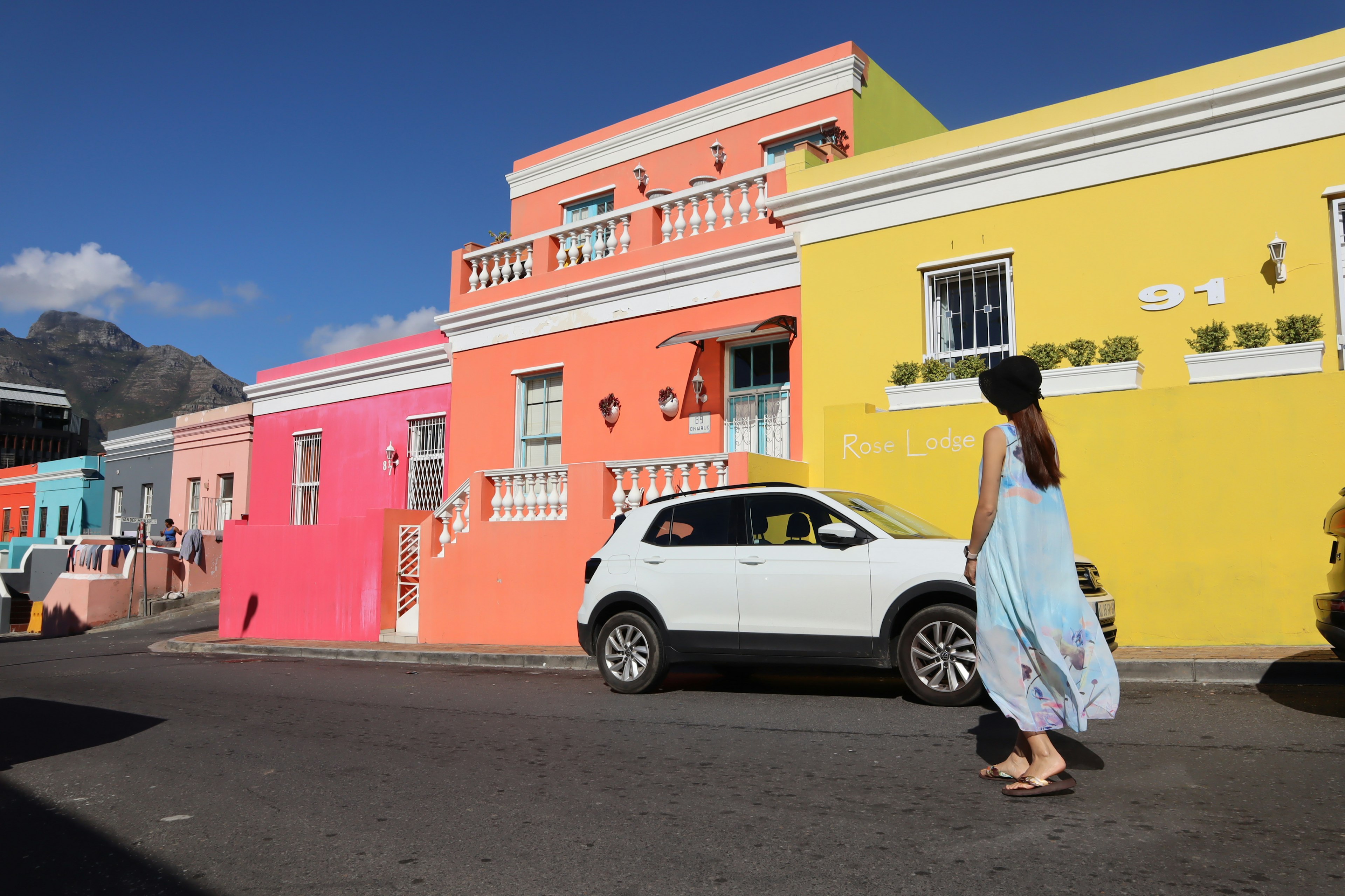 A woman walking past colorful houses with a white car