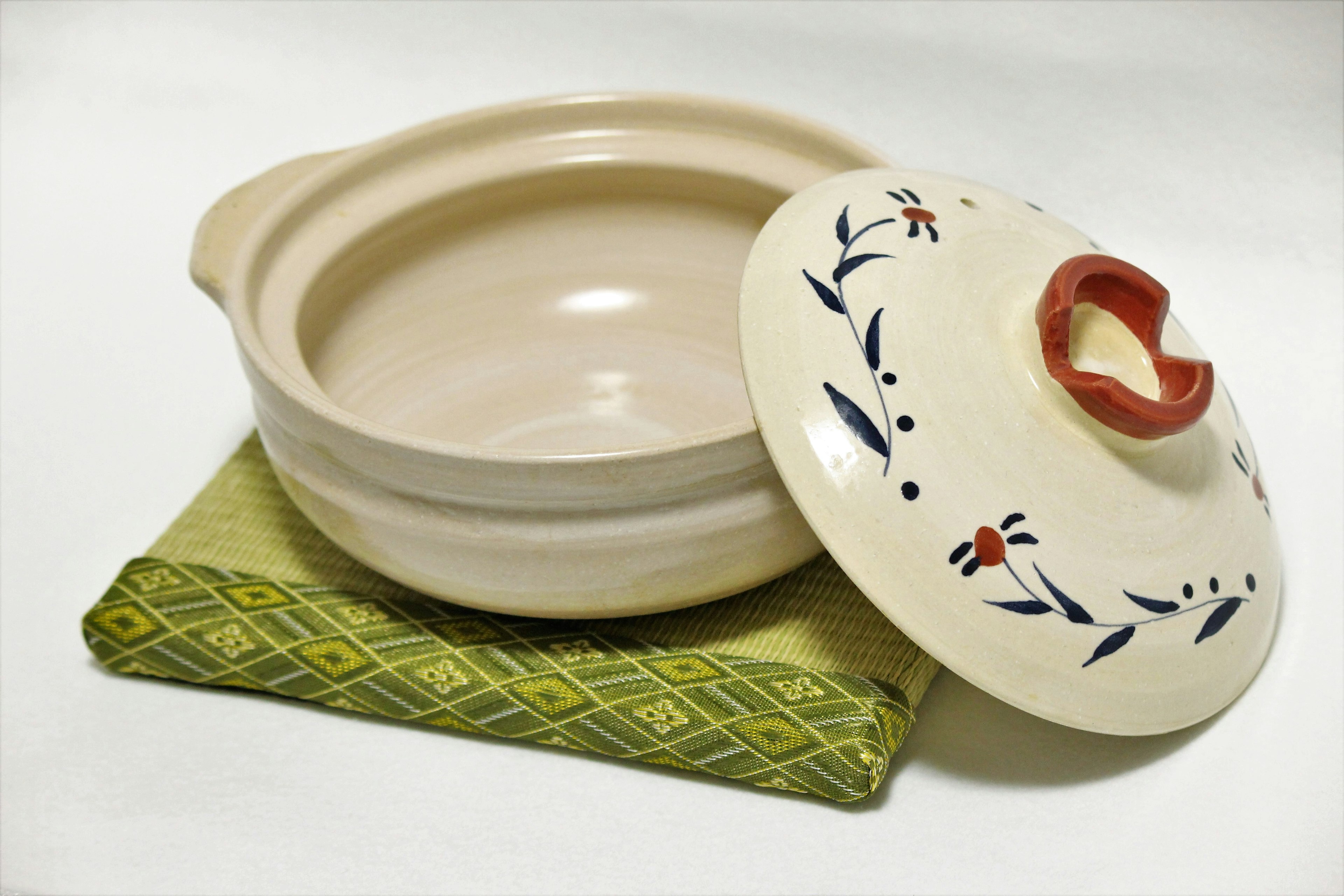 Ceramic pot with lid featuring a red handle placed on a green cloth