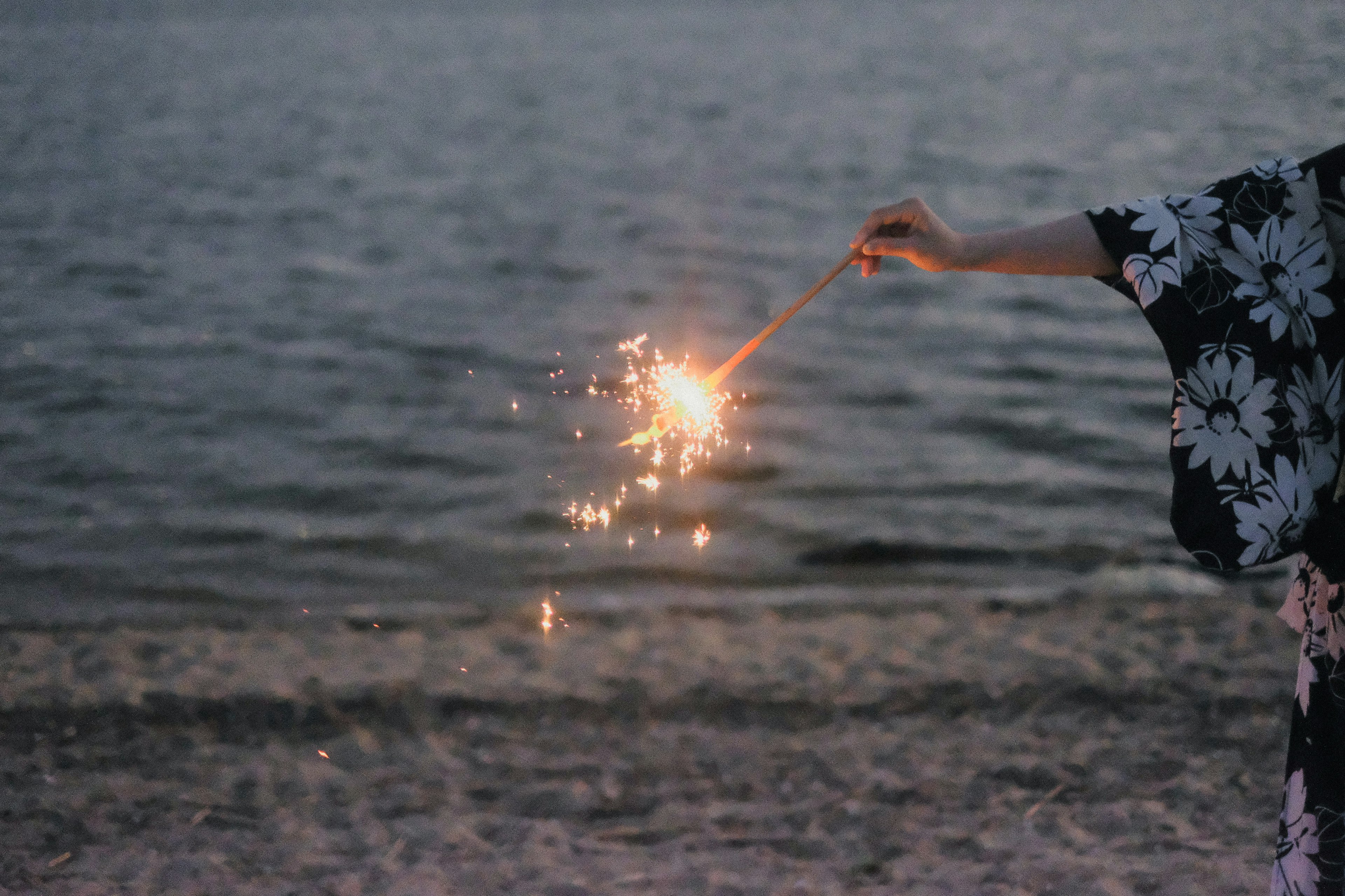 Una mano de mujer sosteniendo un fuego artificial junto al mar