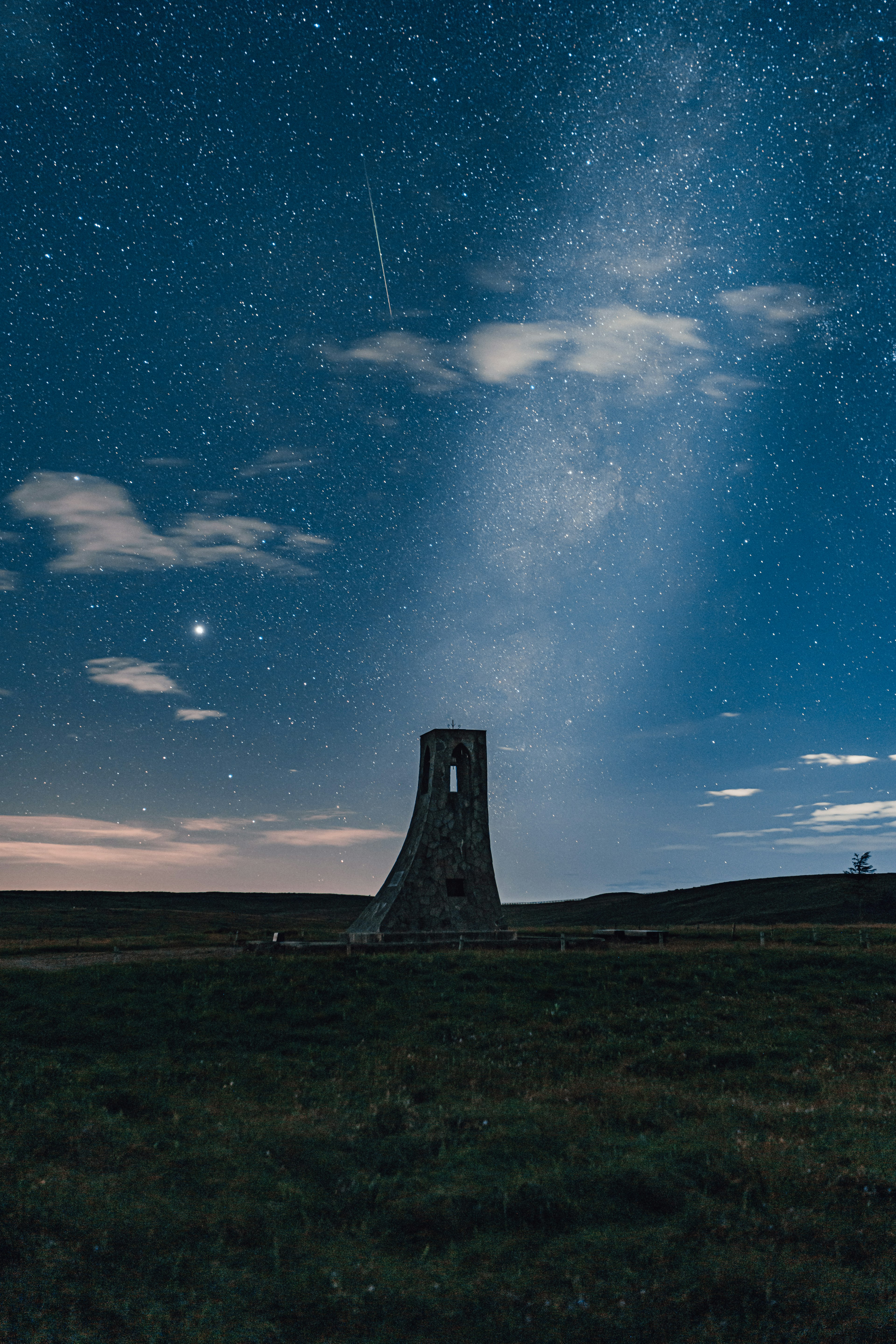 星空の下にある古い塔と流れ星が見える風景