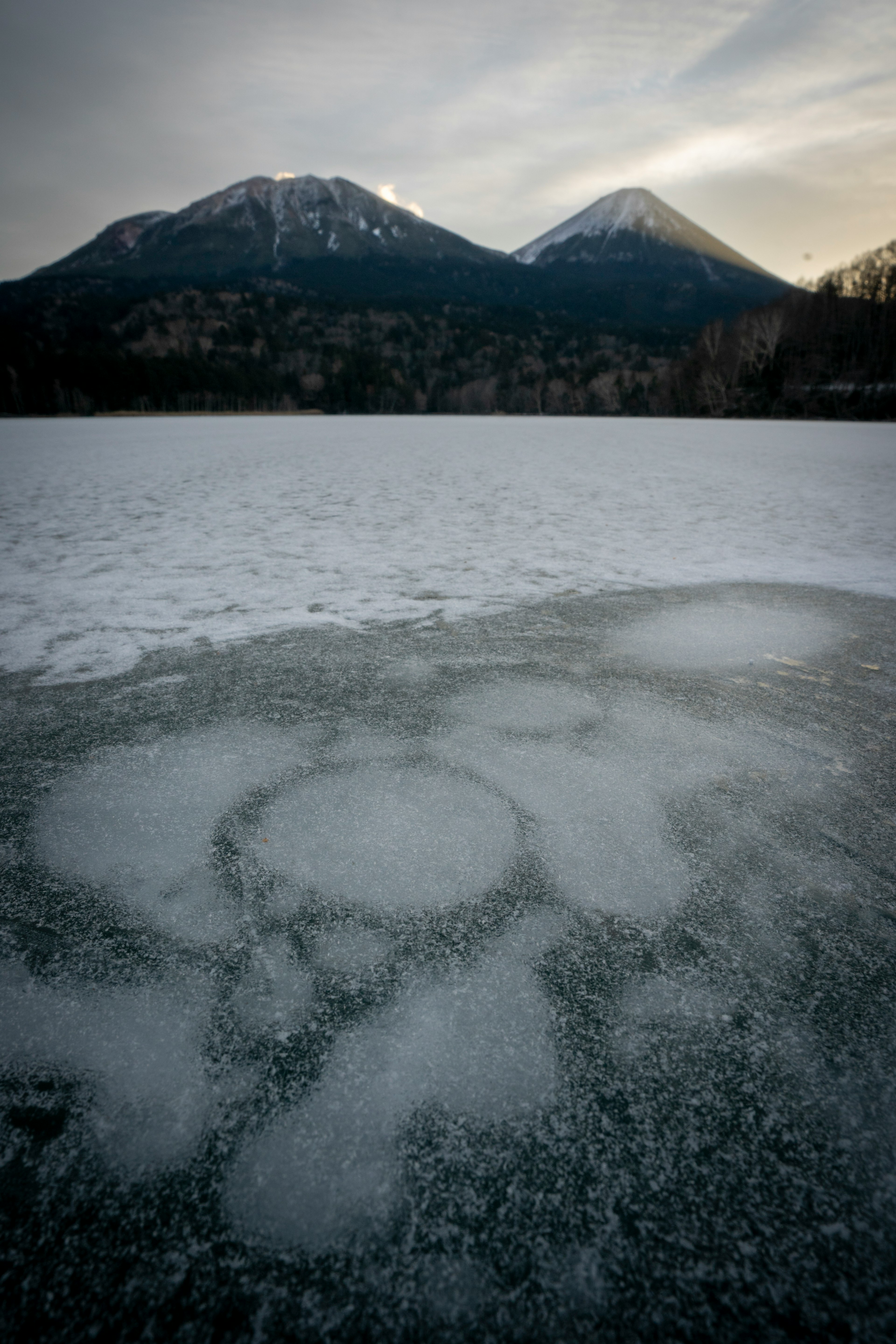 Snow-covered lake with snow-capped mountains in the background circular patterns visible under the ice