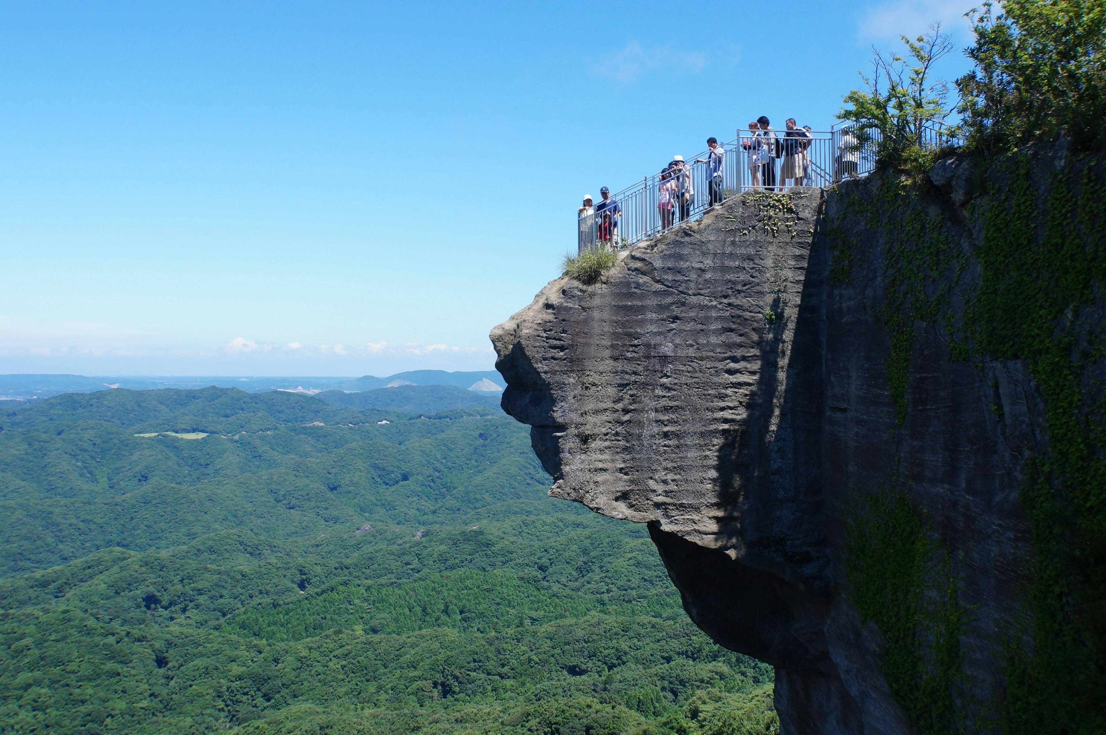 Group of tourists standing at the edge of a cliff with lush green mountains in the background