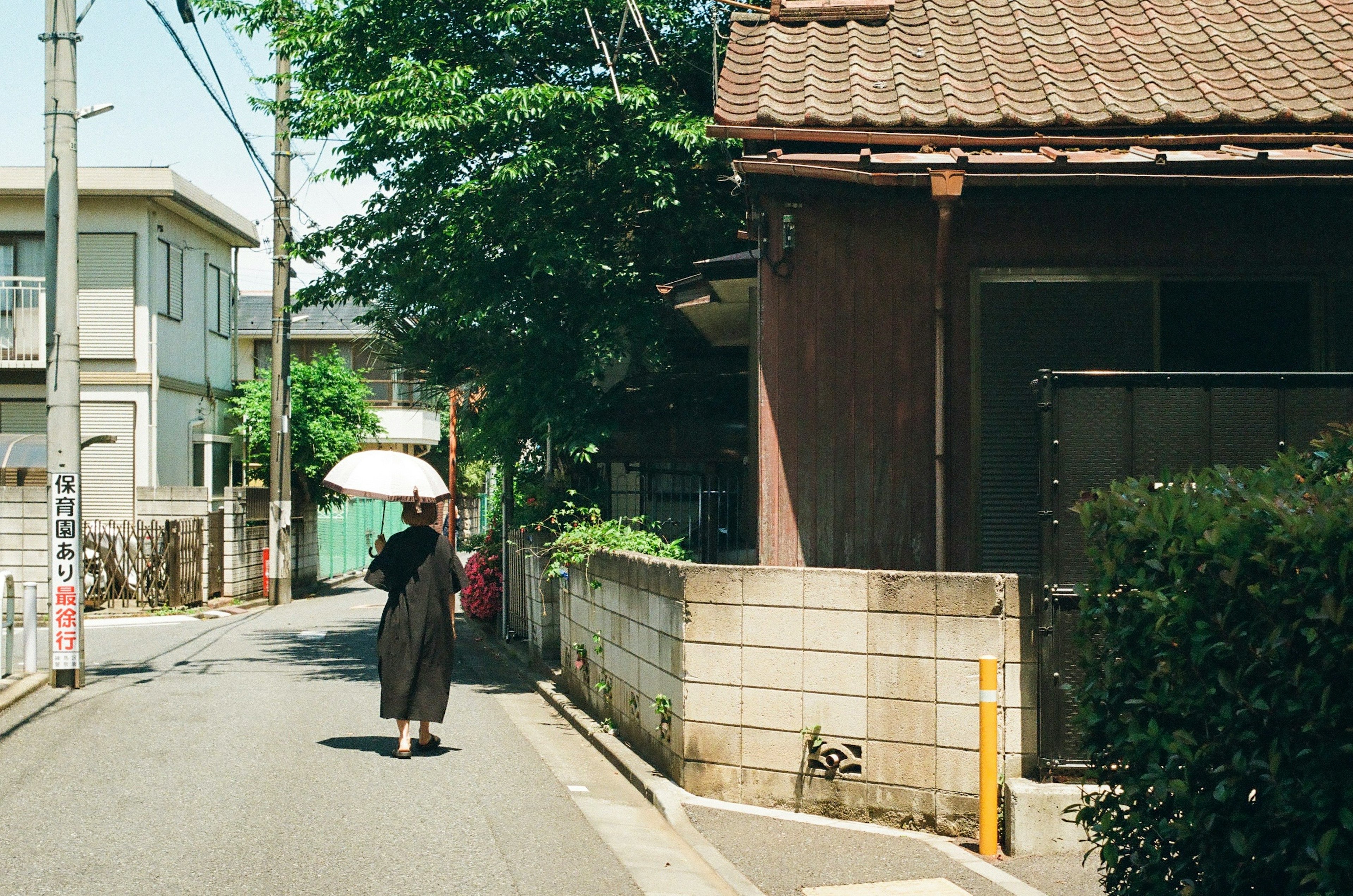 日傘を持った女性が狭い道を歩いている風景