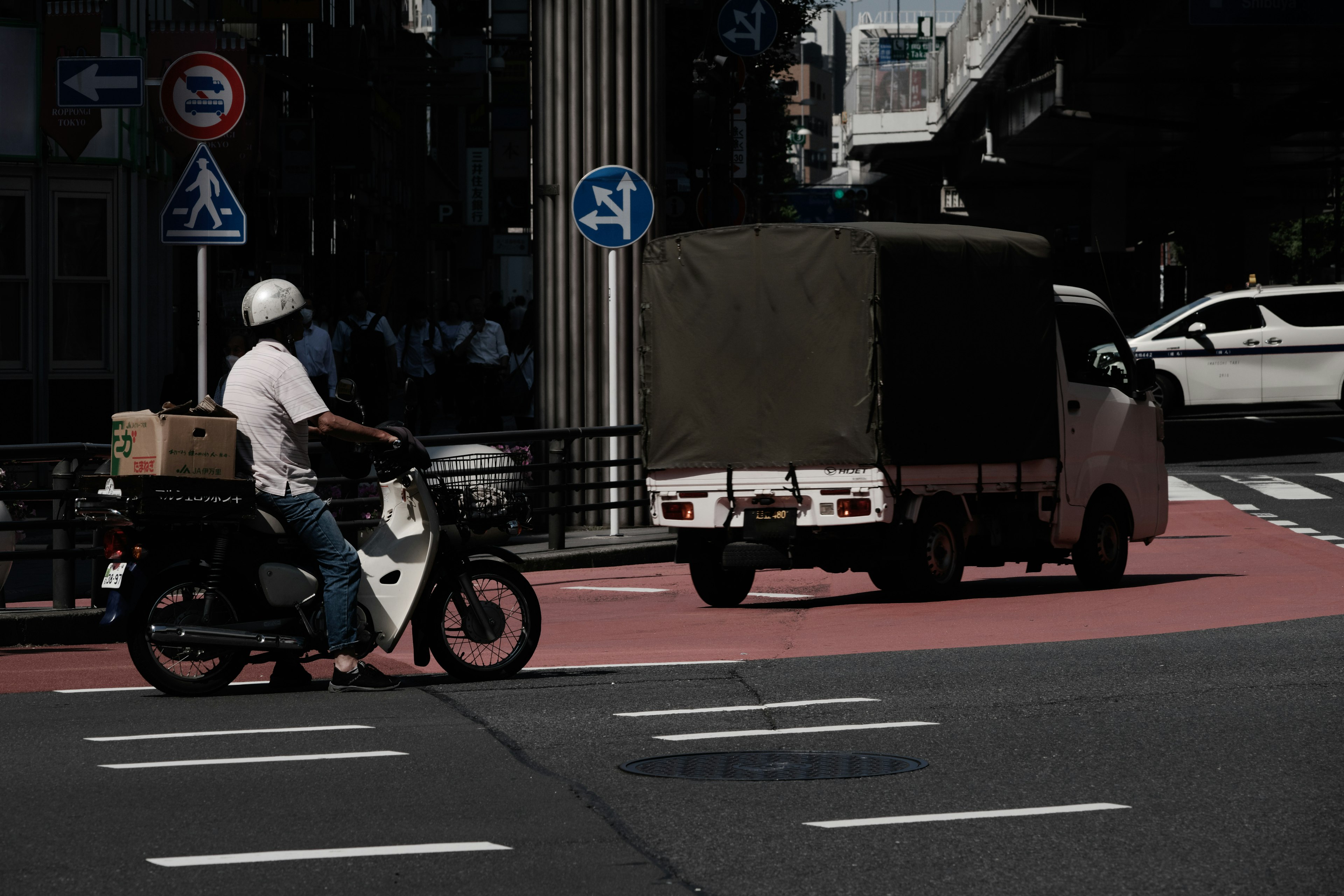 A delivery rider on a motorcycle and a small truck turning at an intersection