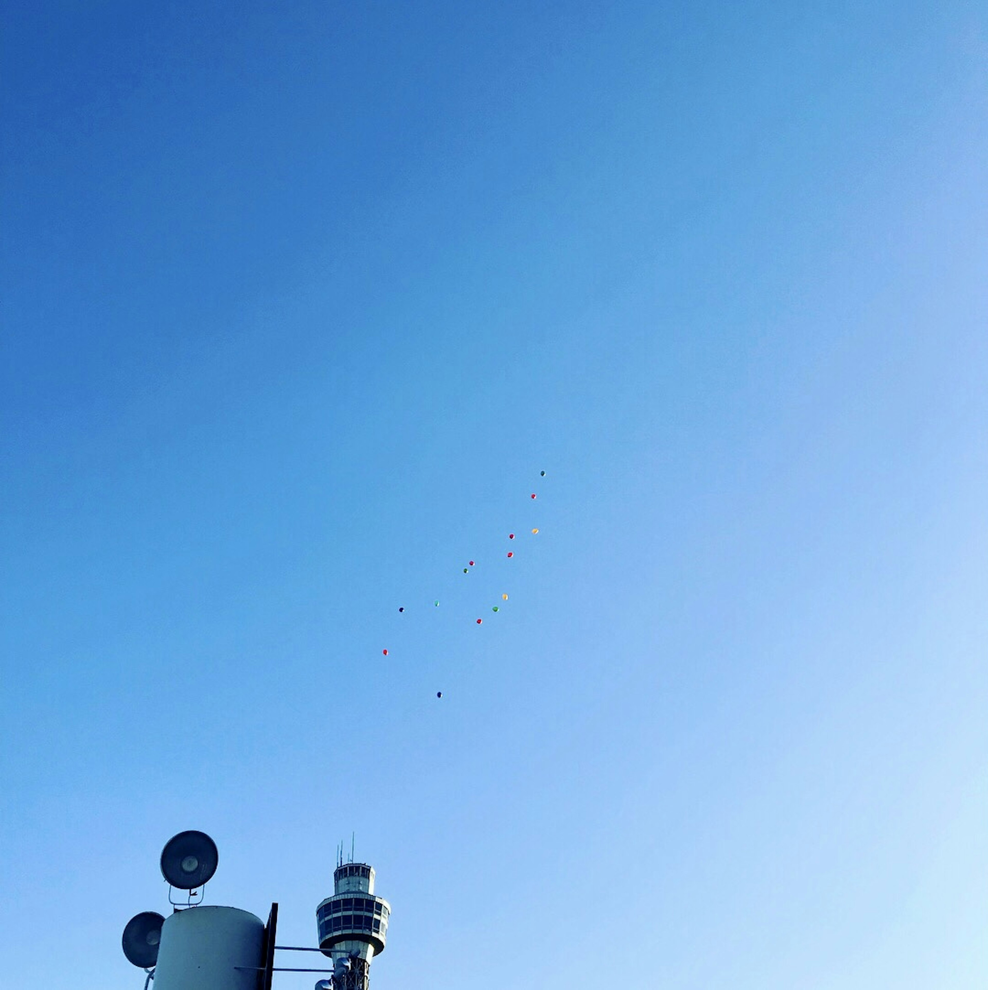 Eine Ansicht von Ballons, die im blauen Himmel mit einem Kommunikationsturm schweben