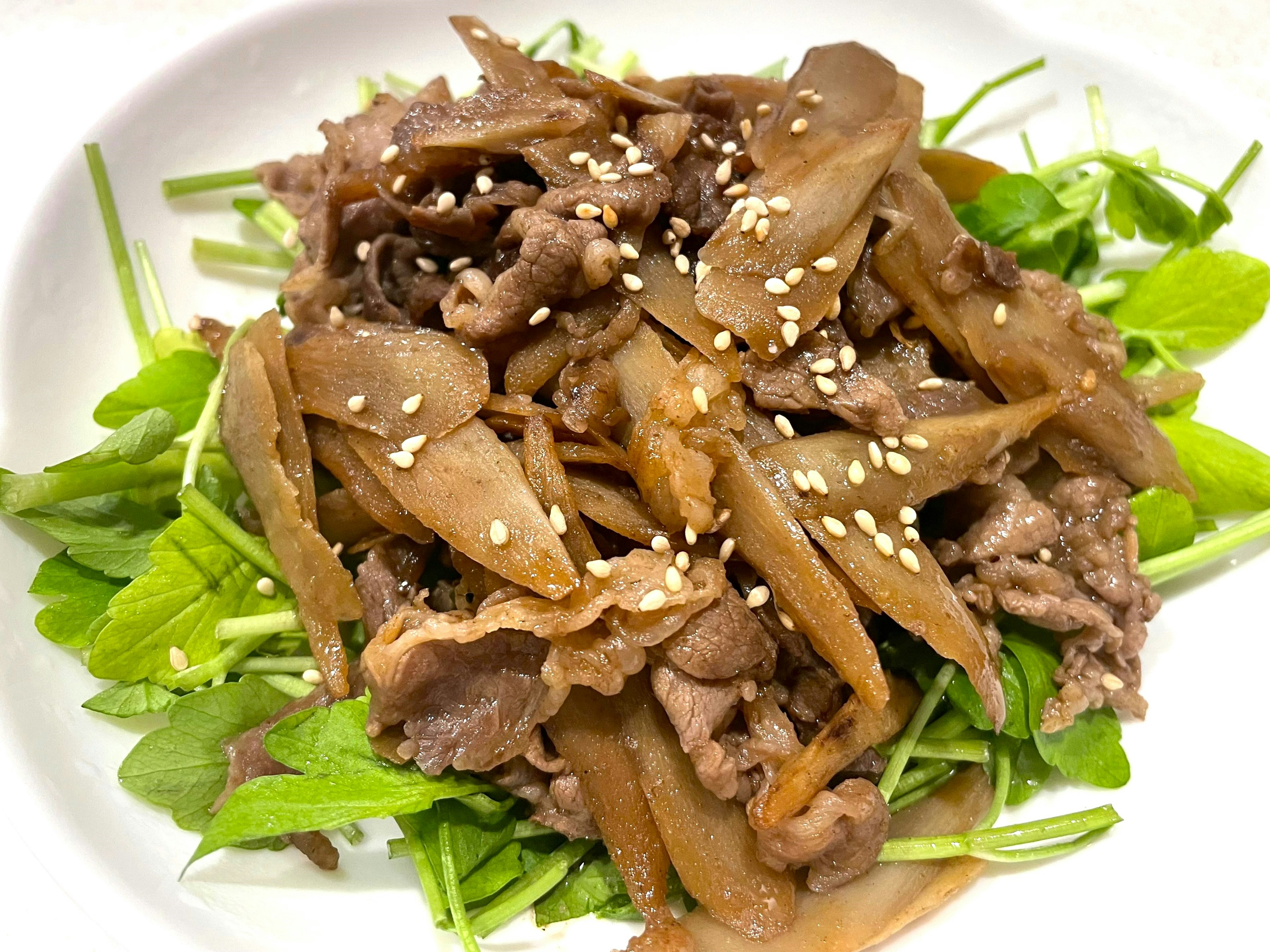 A meat dish served on a bed of green vegetables topped with sesame seeds