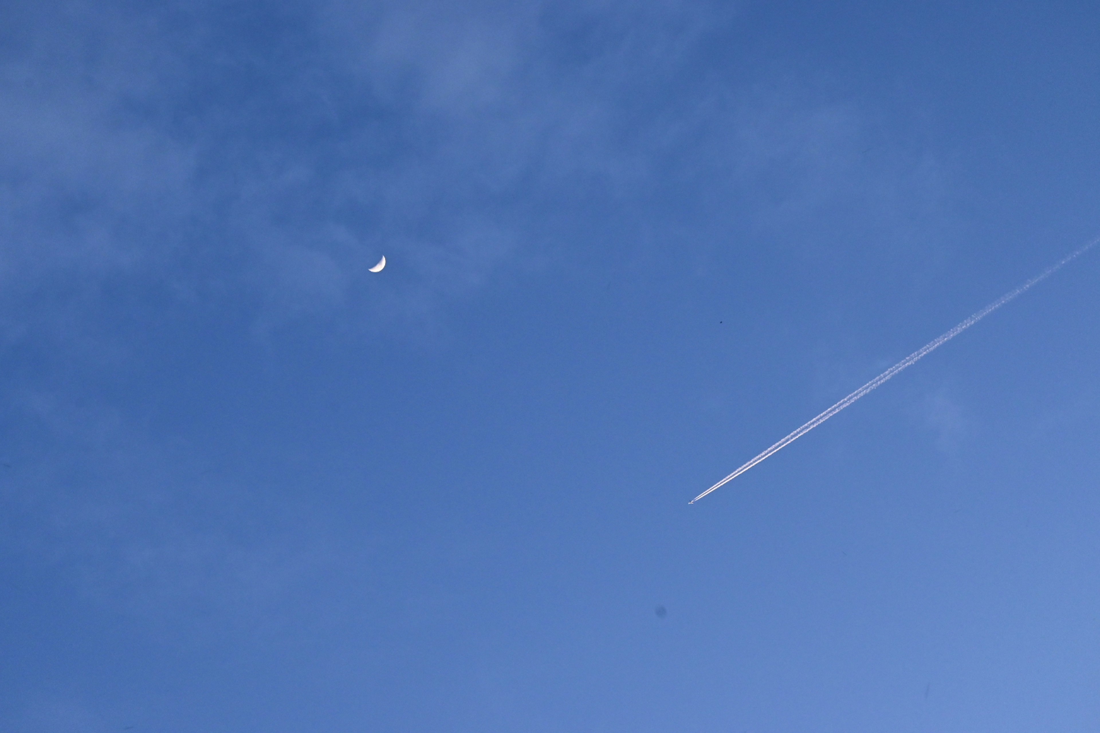 Moon in the blue sky with a contrail