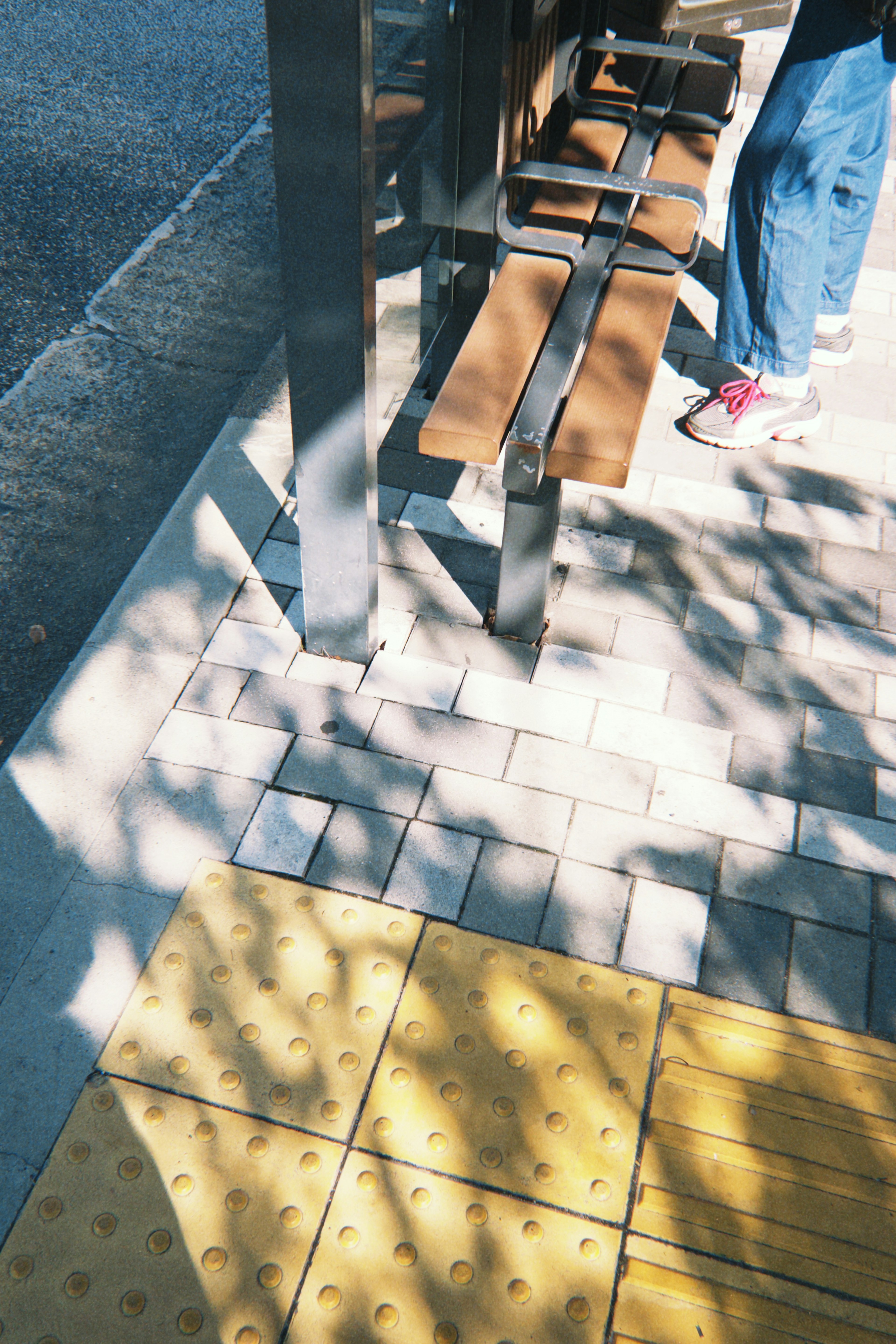 Foto de una acera con un banco y sombras