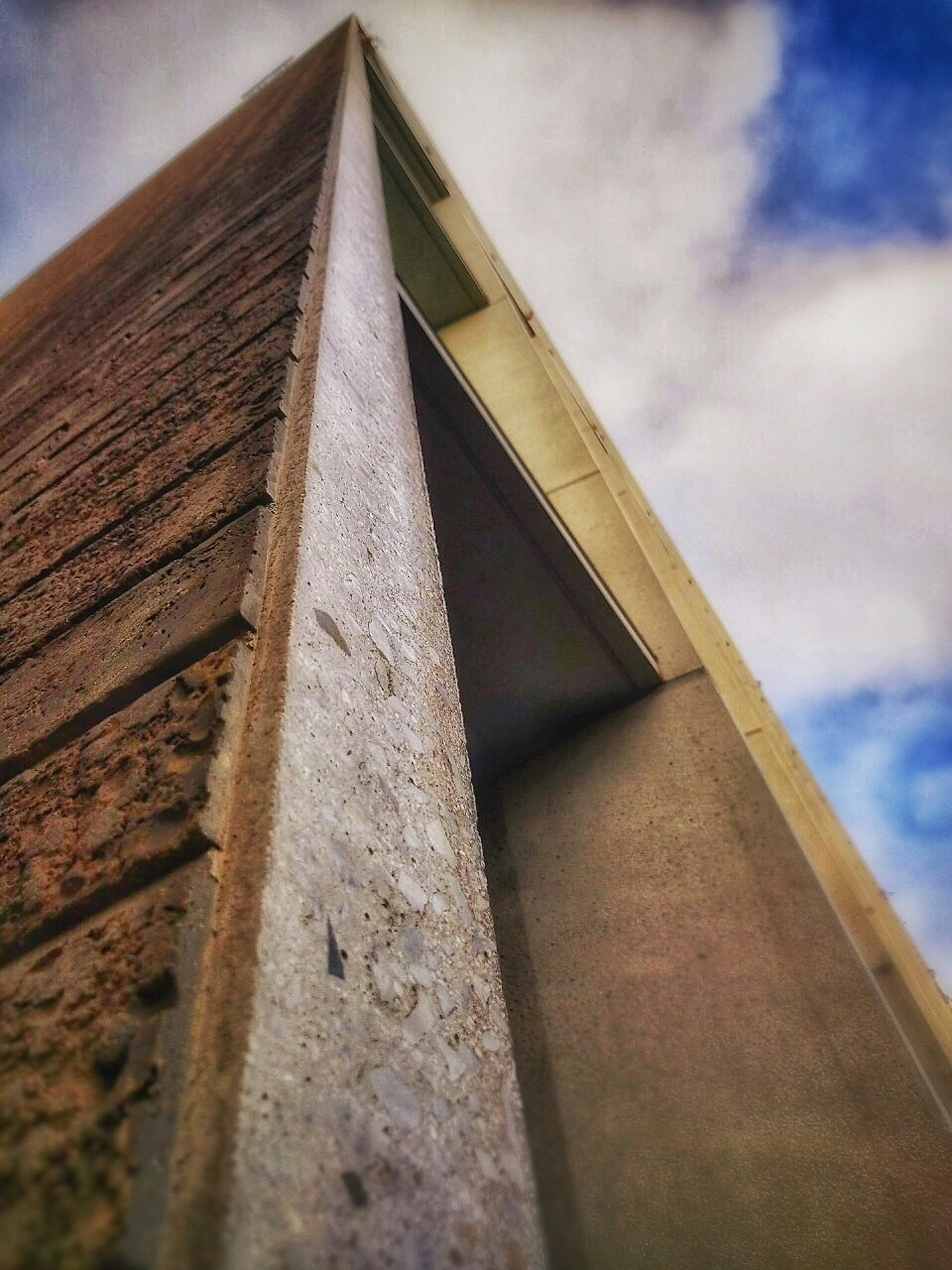 Imagen de la esquina de un edificio vista desde abajo con cielo azul y nubes de fondo