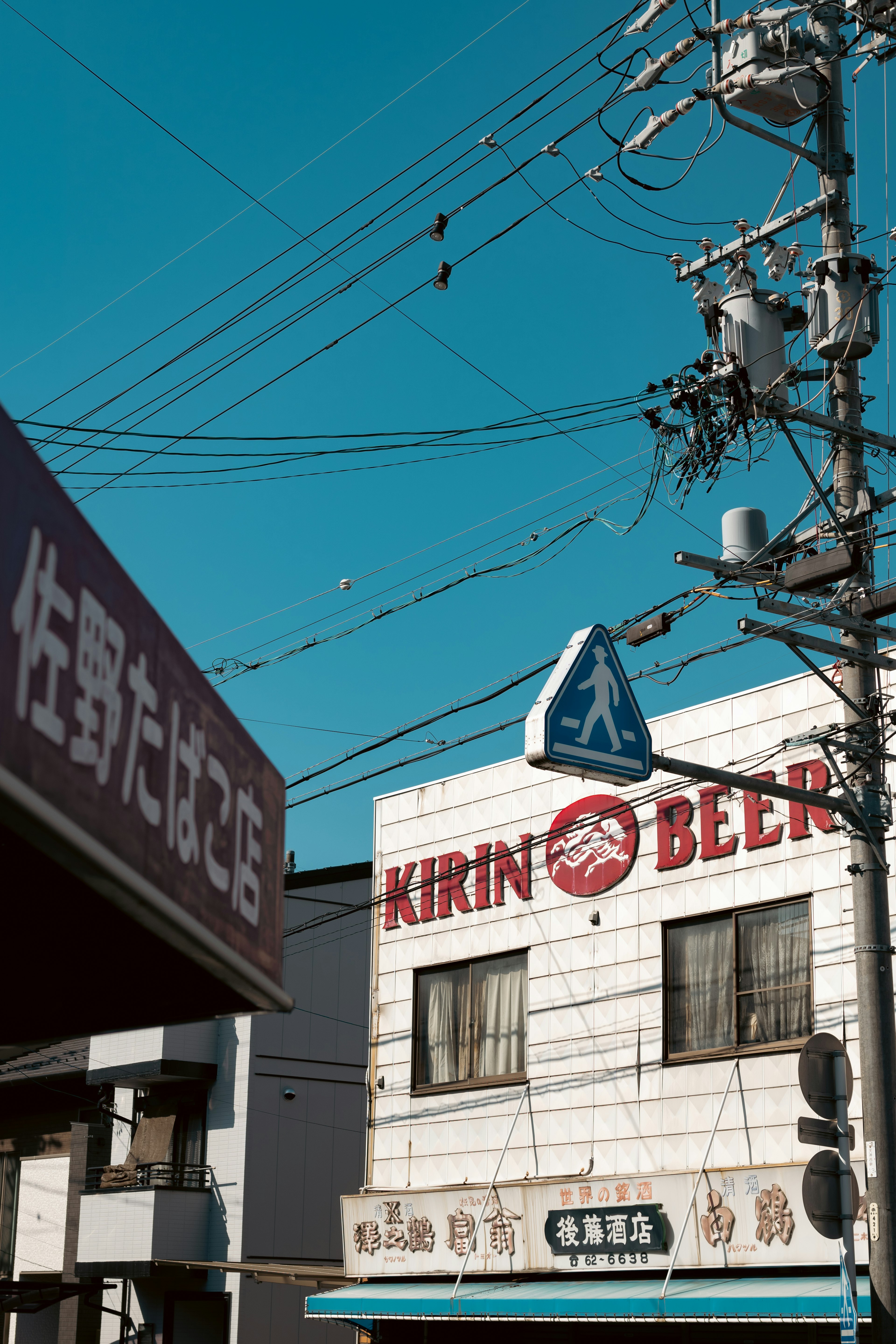 Escena de calle con un letrero de Kirin Beer bajo un cielo azul y postes eléctricos