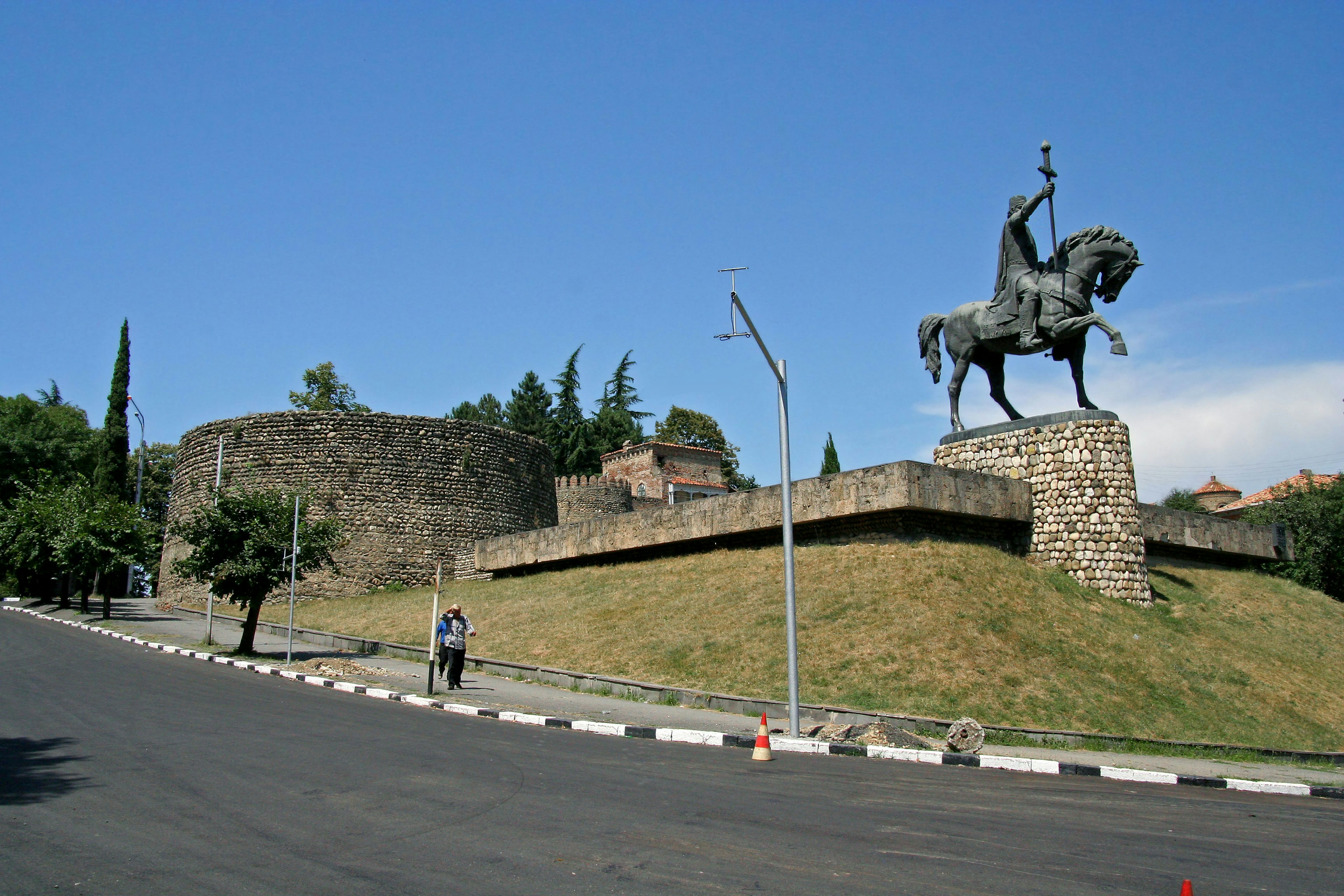 Una estatua de caballero a caballo con un muro de piedra al fondo bajo un cielo azul