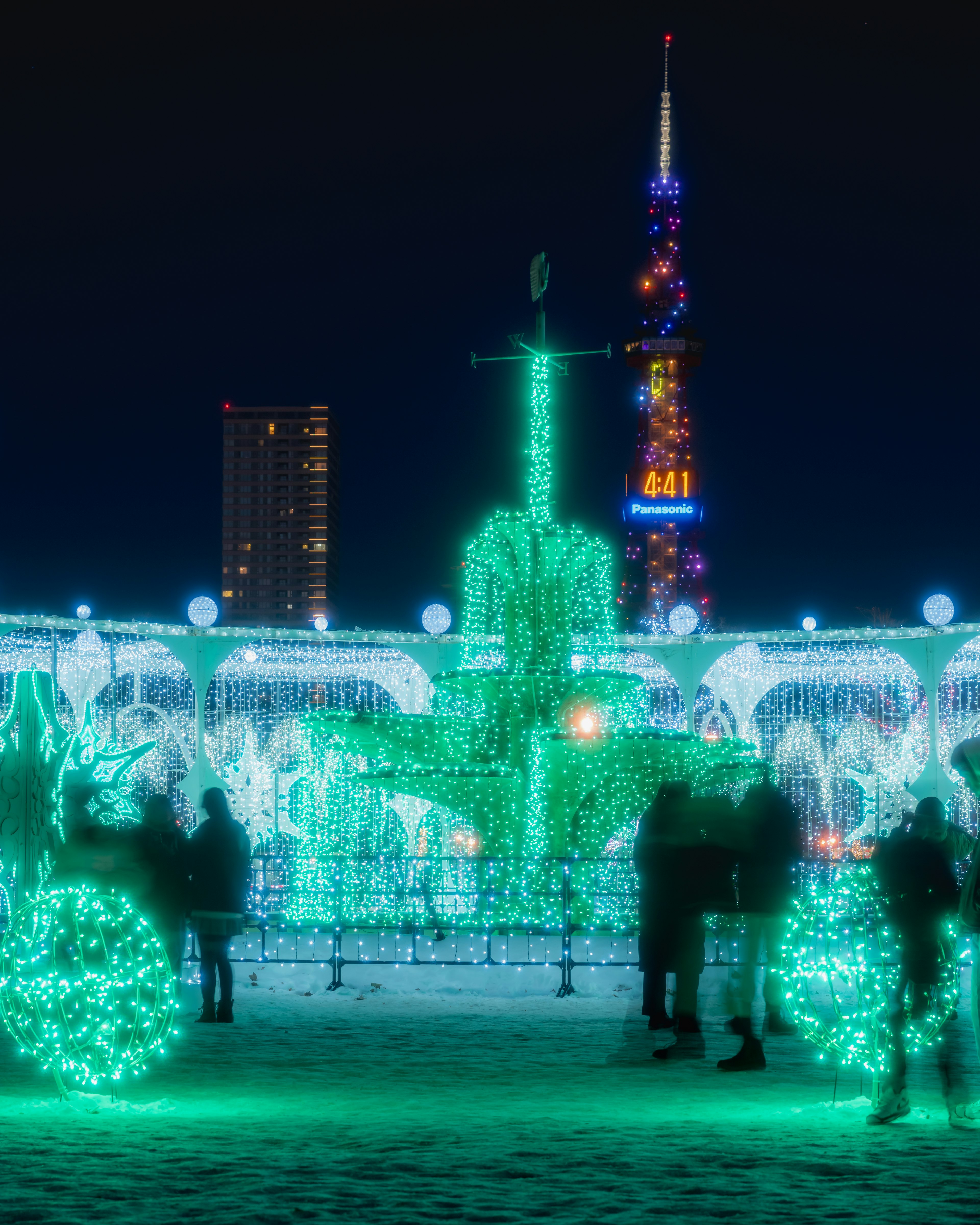 People standing in a plaza decorated with green lights at night