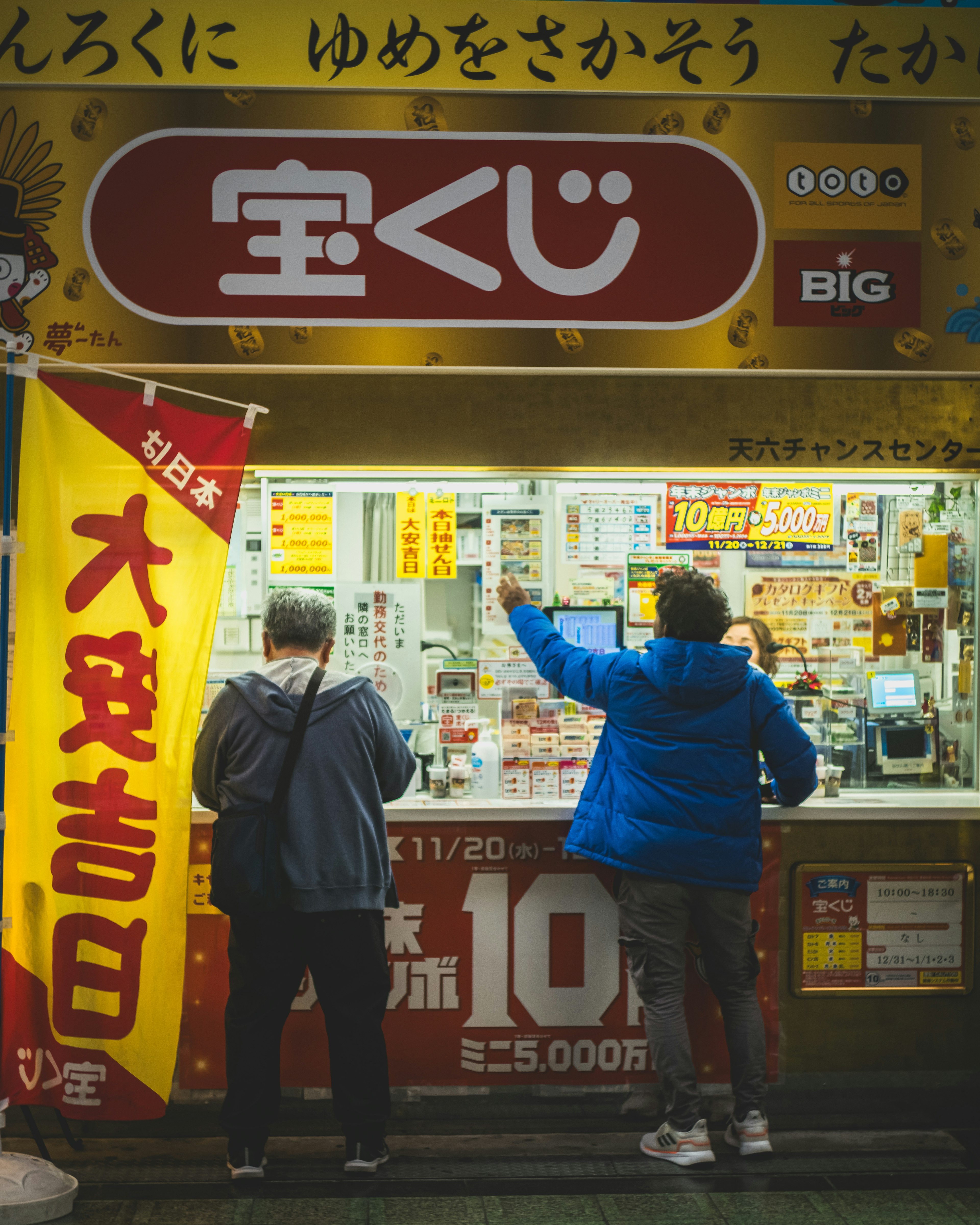 People purchasing lottery tickets at a lottery booth man in blue jacket and woman in black clothing