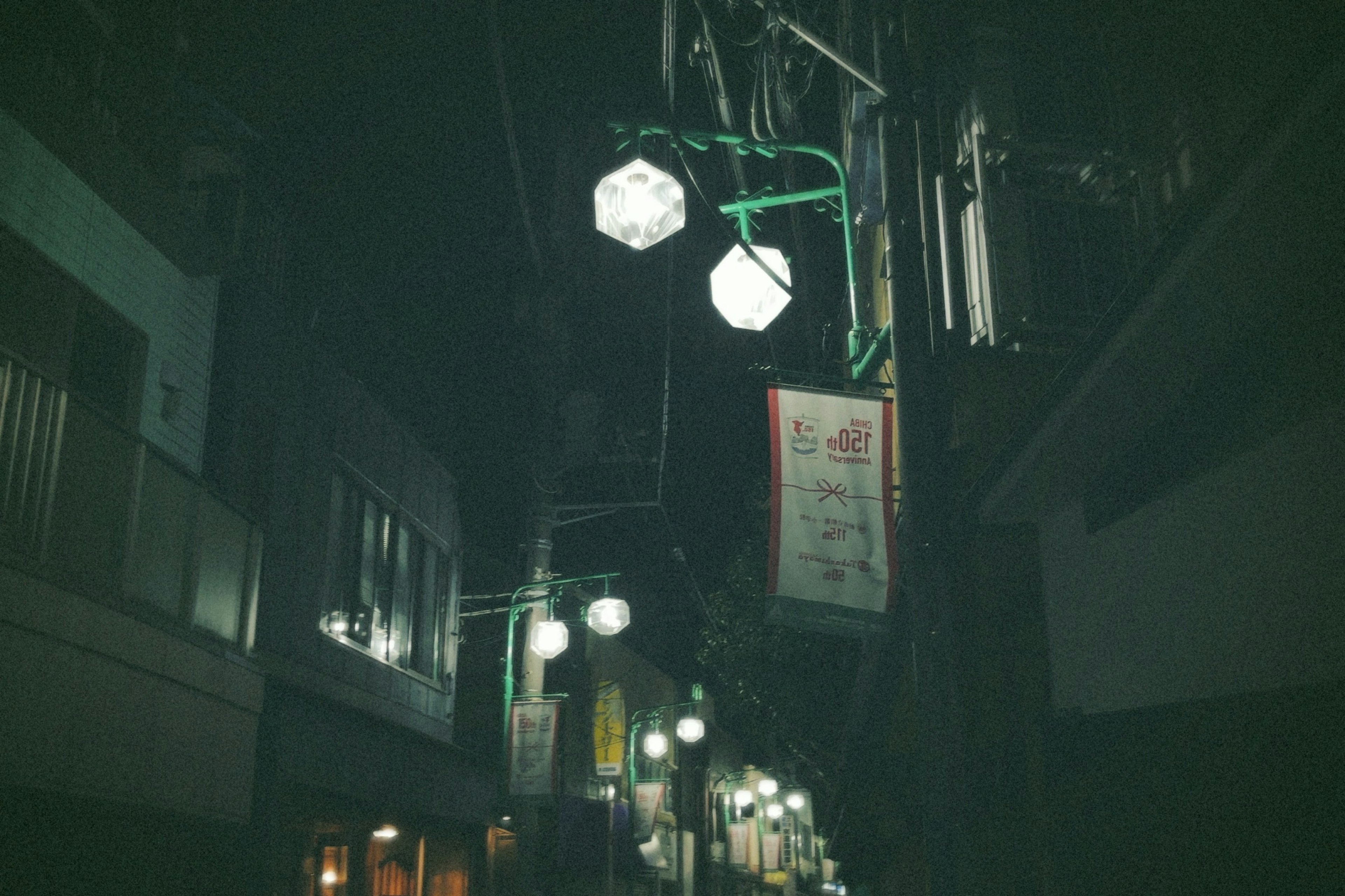 Schmale Straße bei Nacht mit hängenden Laternen und Schildern