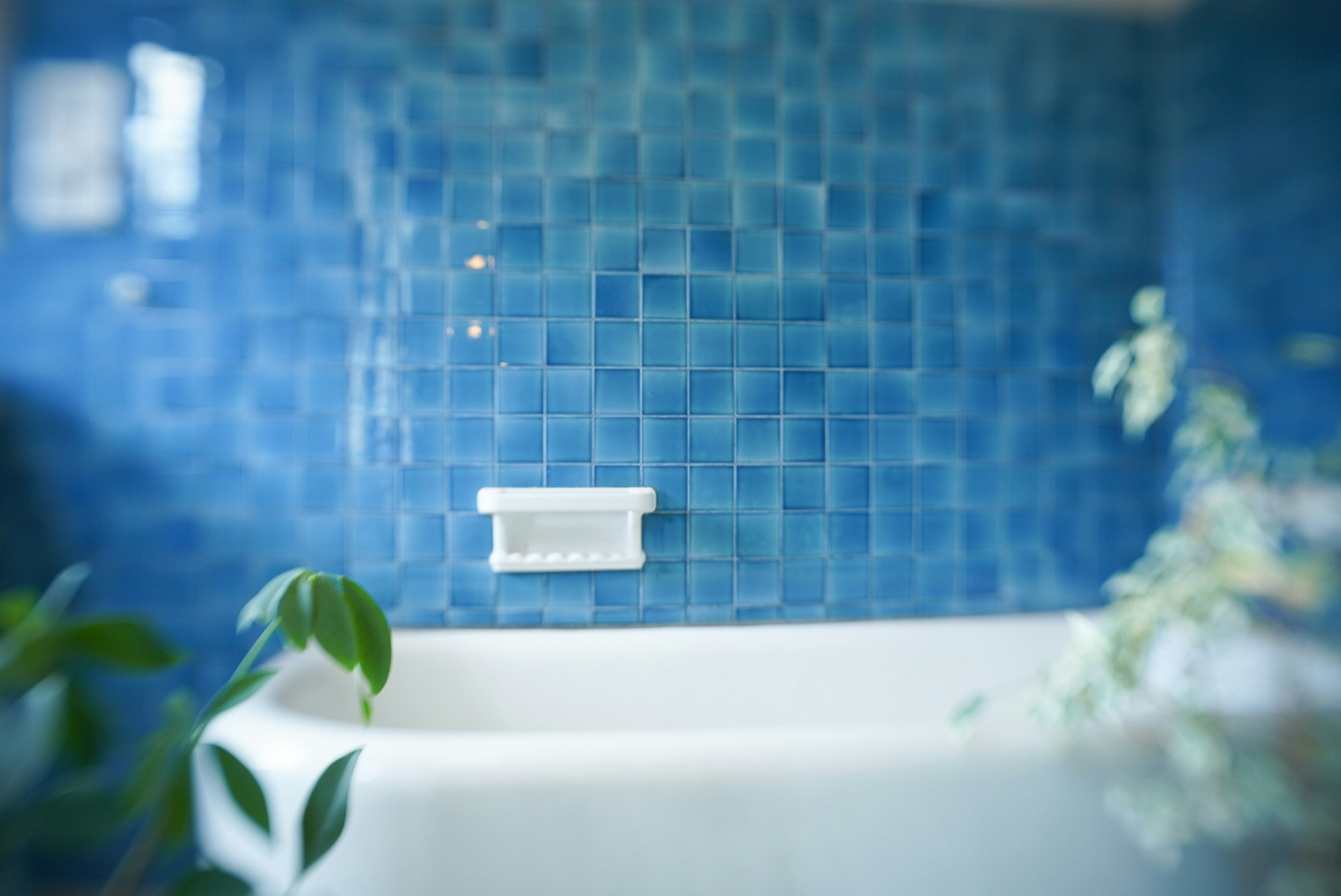 Image of a bathroom wall with blue tiles and a white bathtub