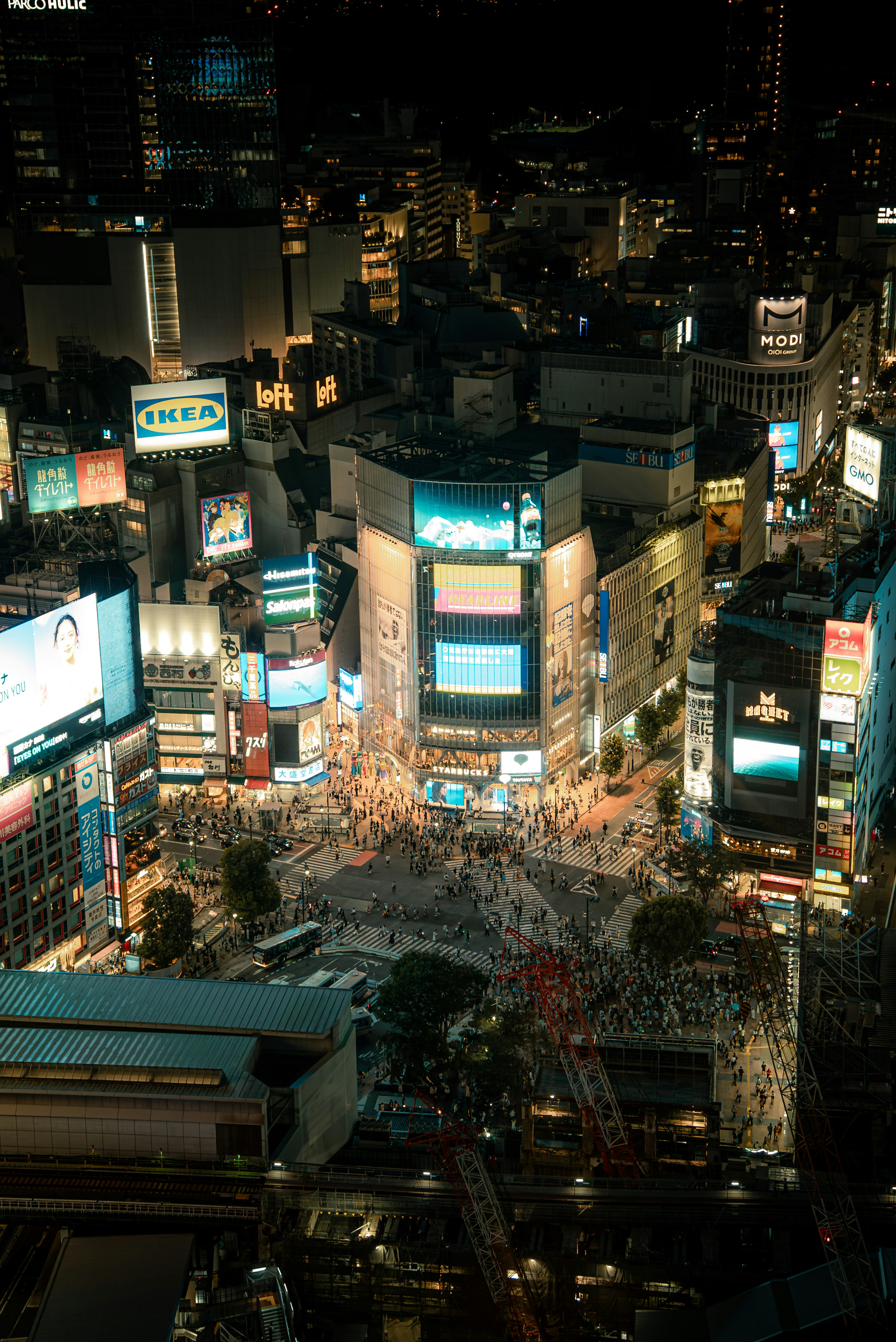 Aerial view of Shibuya Crossing at night featuring bright neon lights and advertisements