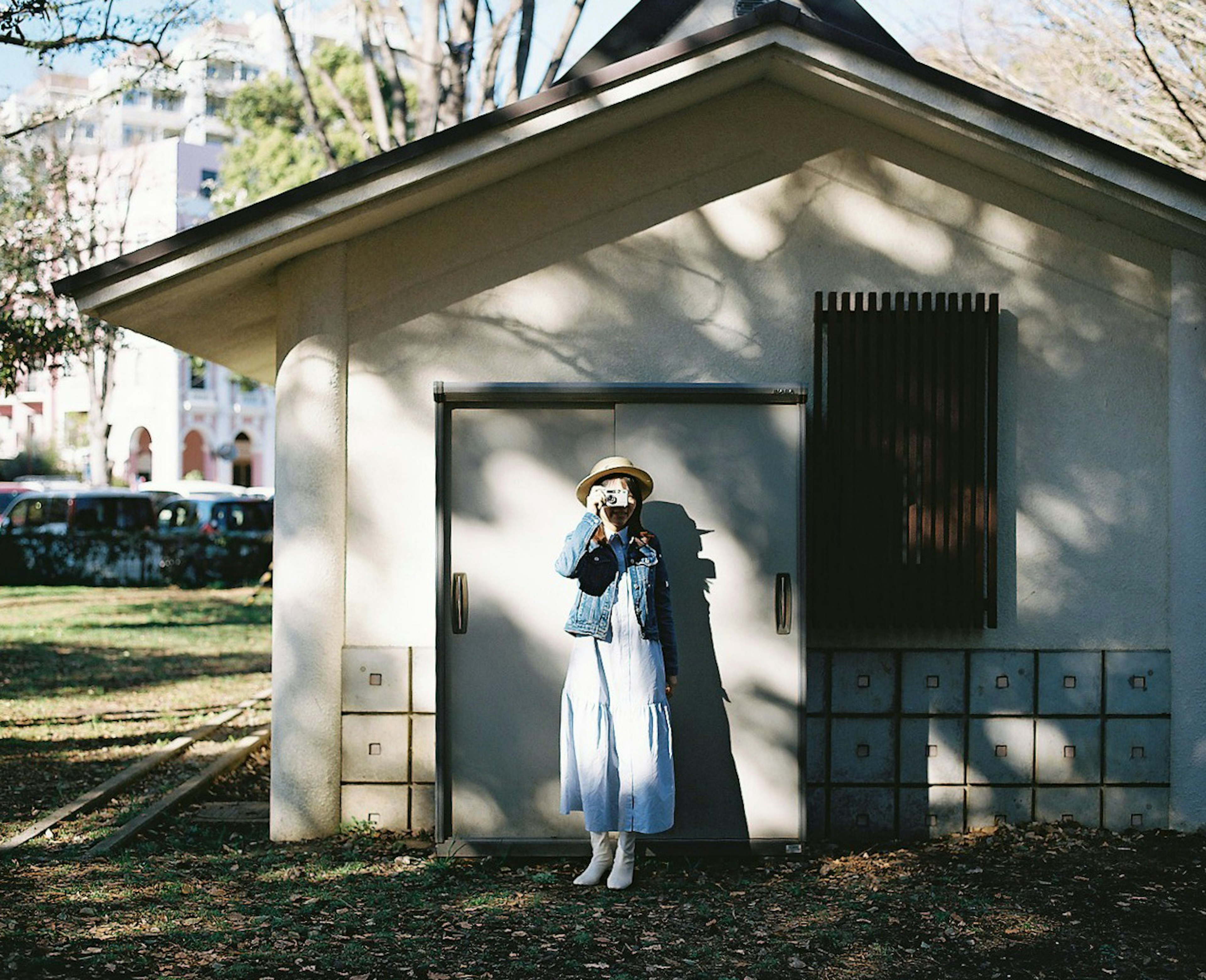 公園の小屋の前に立つ女性 白いドレスとデニムジャケットを着たスタイル