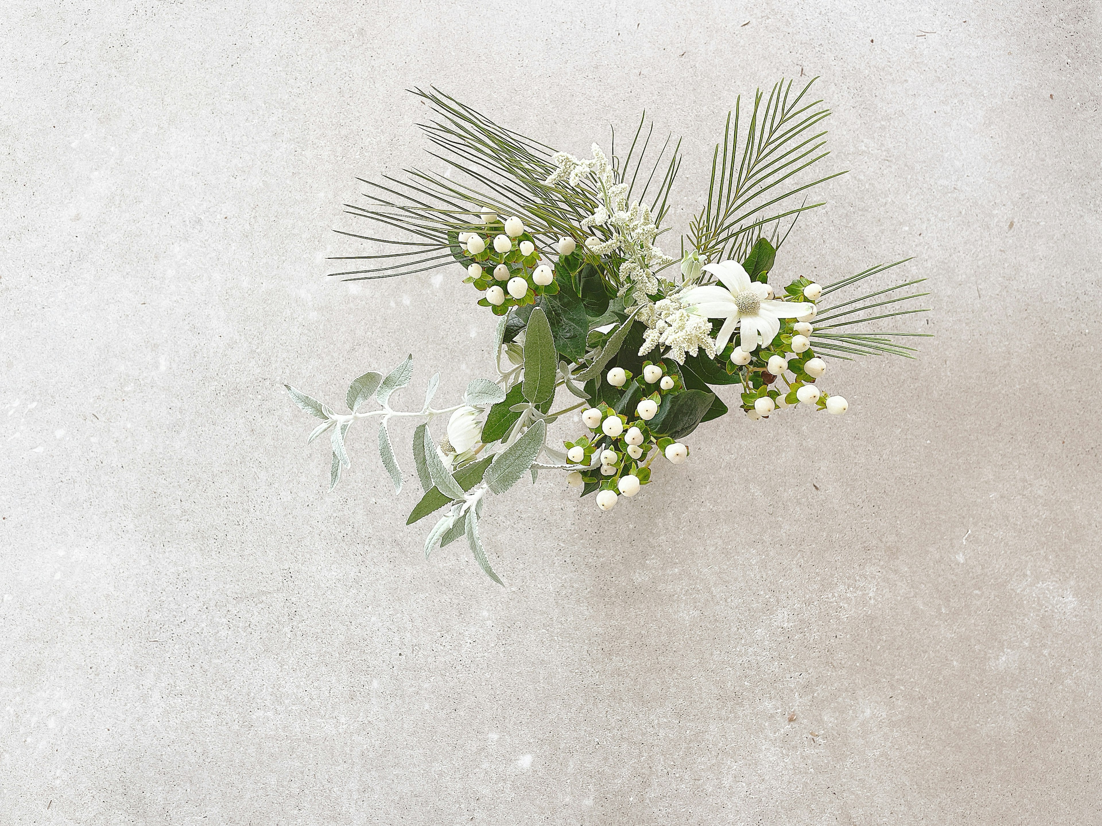 Un hermoso ramo de flores blancas y hojas verdes dispuesto sobre un fondo gris