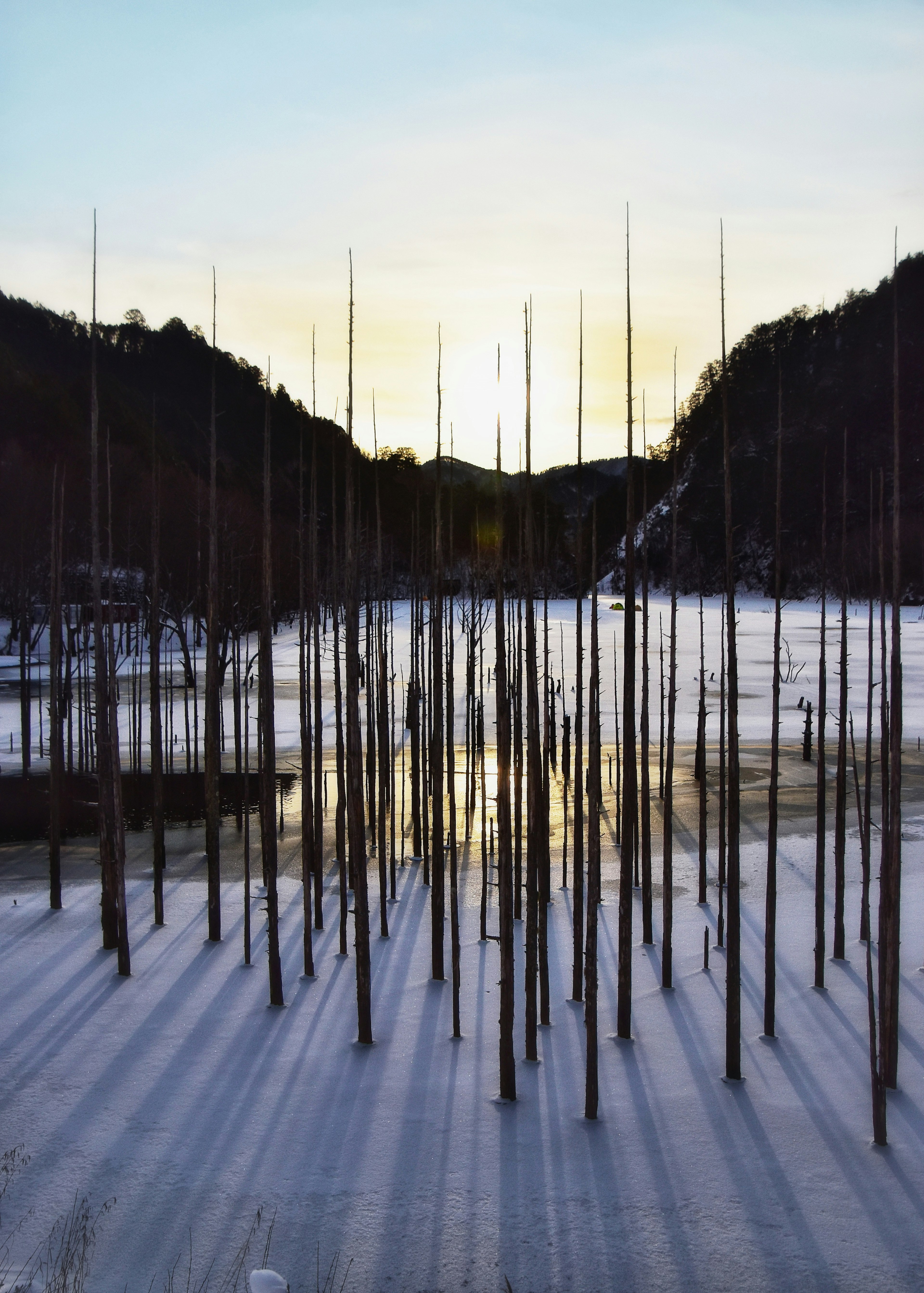 Lago ghiacciato con pali in piedi e paesaggio al tramonto