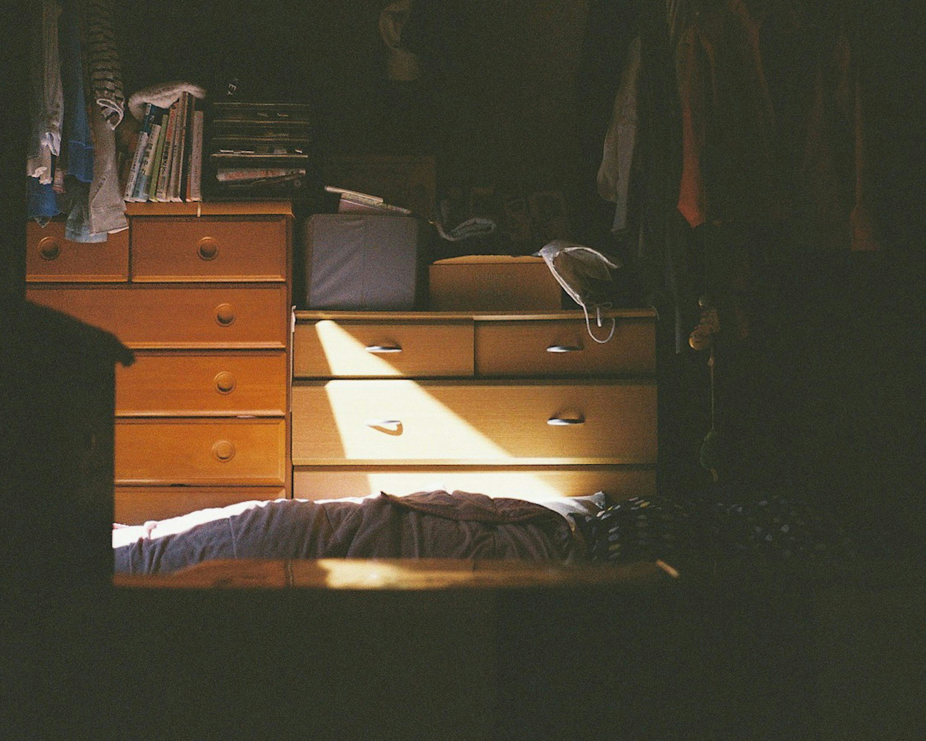 Soft light illuminating a bed and wooden drawers in a dim room