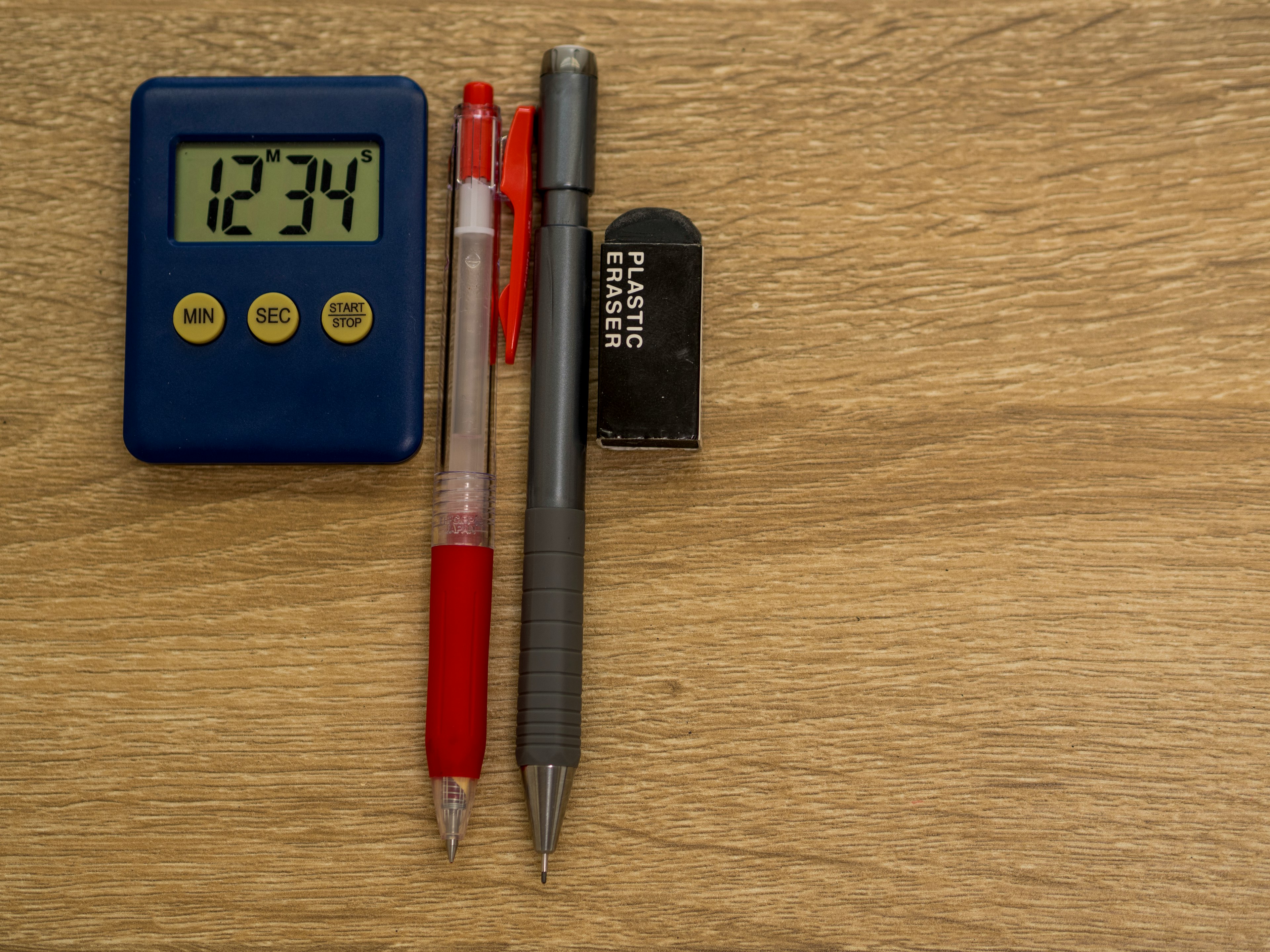 Un chronomètre numérique bleu à côté d'un stylo rouge, d'un stylo gris et d'une gomme noire sur une table en bois