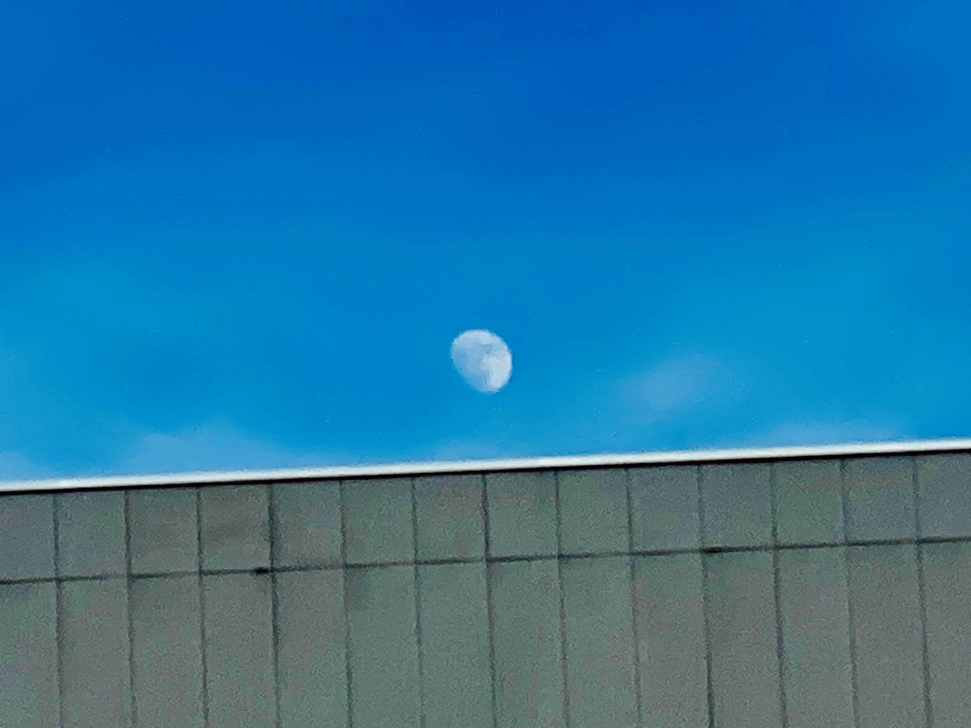 Luna visible contra un cielo azul claro sobre un techo de edificio