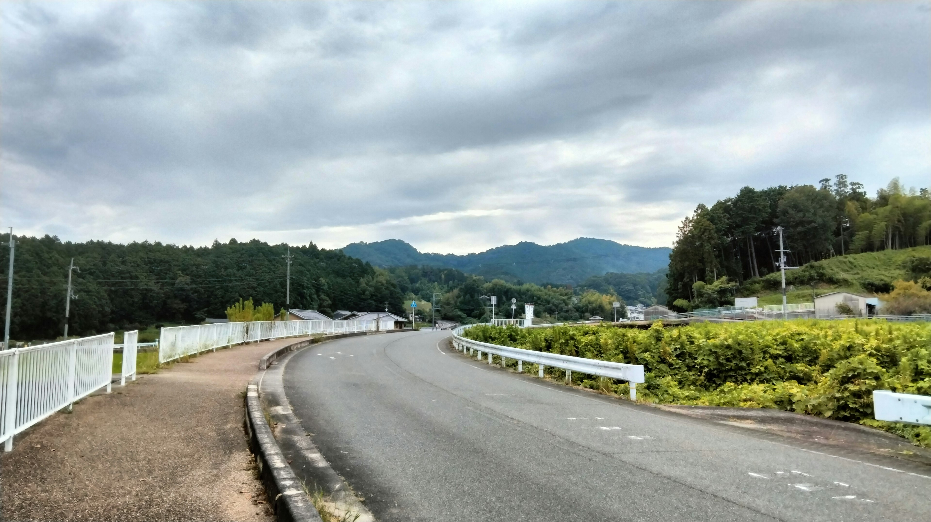 Jalan berkelok dengan bukit hijau dan gunung di latar belakang