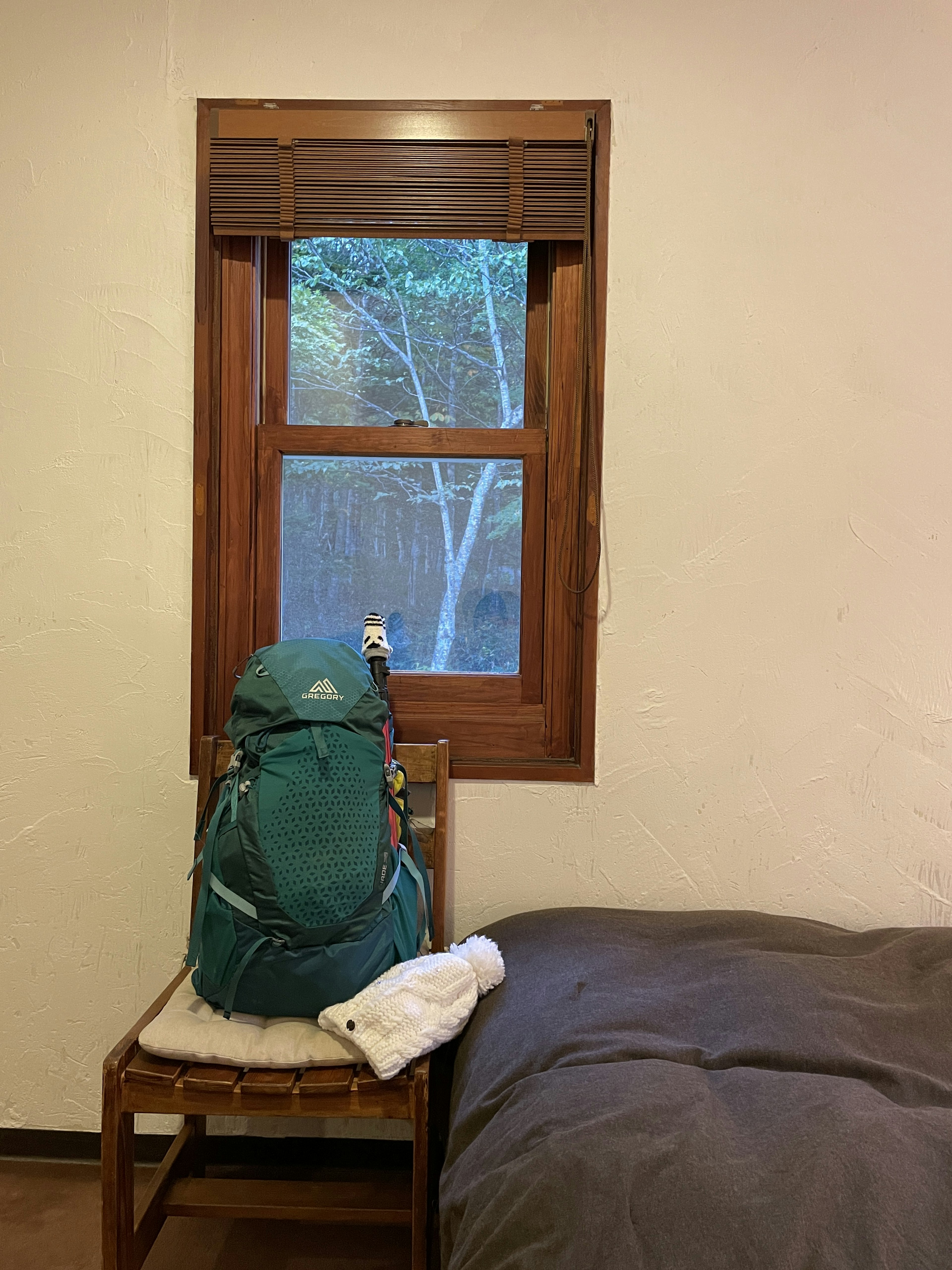 Un sac à dos vert posé sur une chaise avec une vue sur des arbres à l'extérieur de la fenêtre