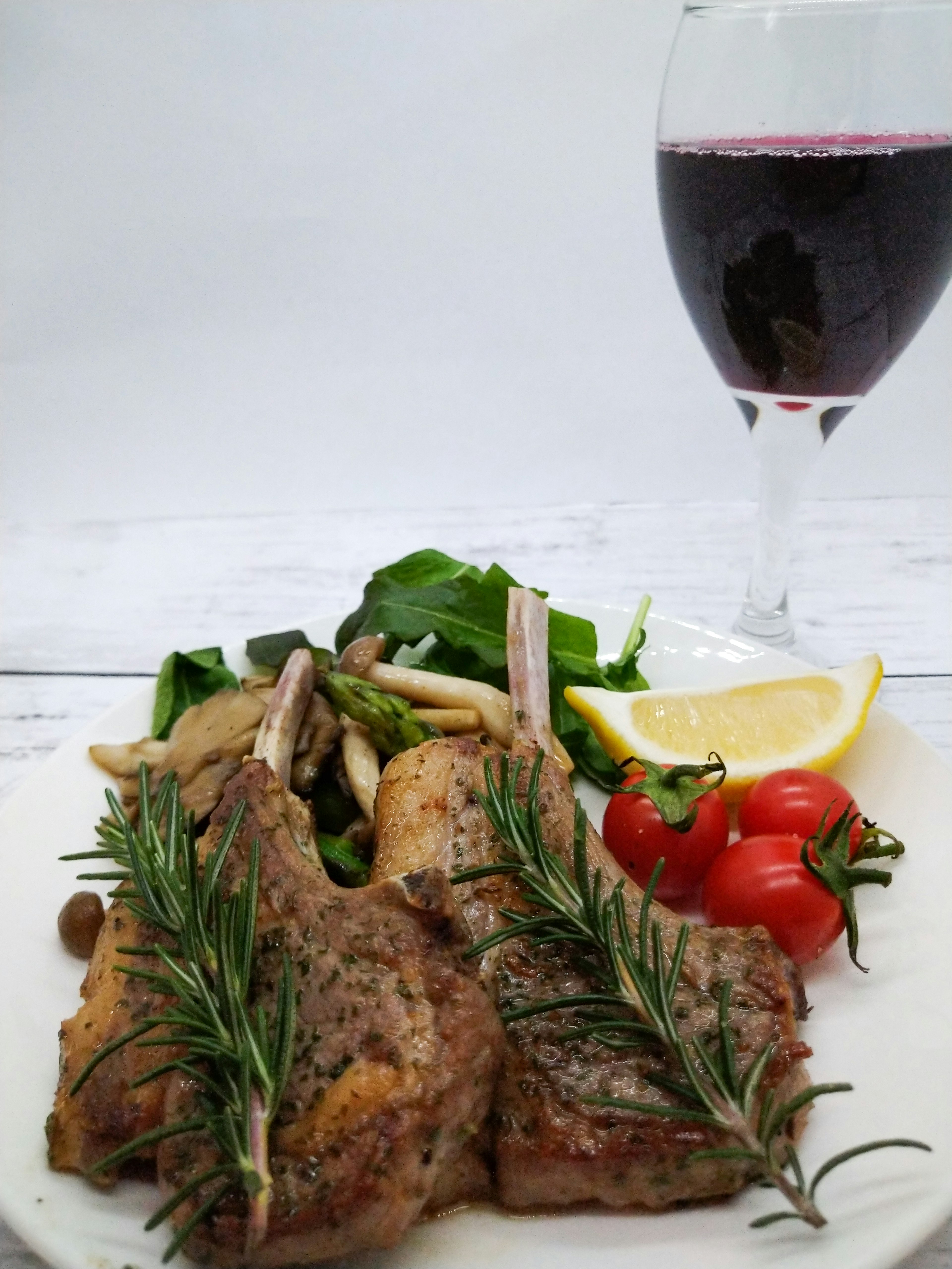 Plate of delicious lamb chops garnished with rosemary alongside a glass of red wine