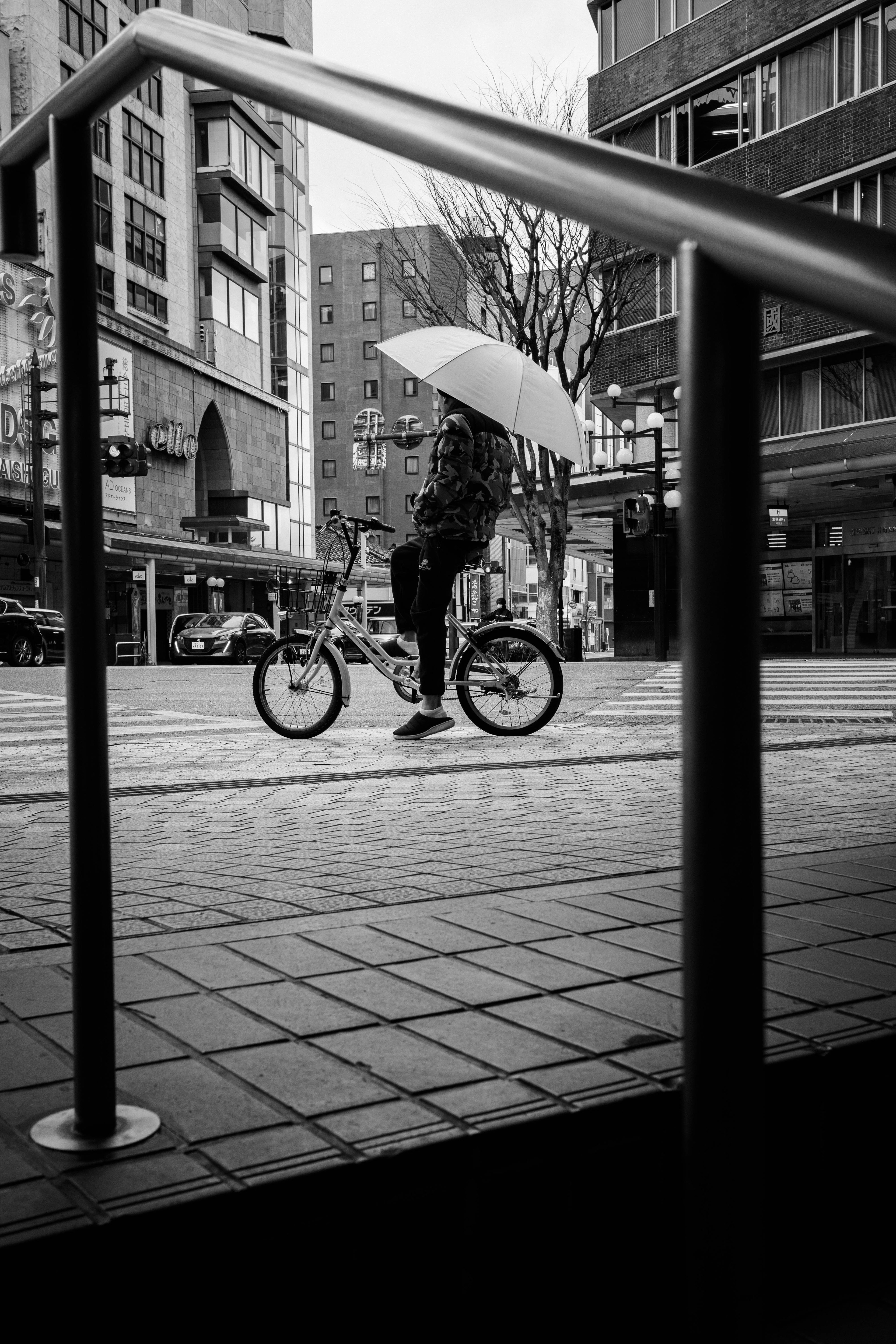 Eine Person, die mit einem Fahrrad und einem Regenschirm in einer monochromen Stadtumgebung fährt