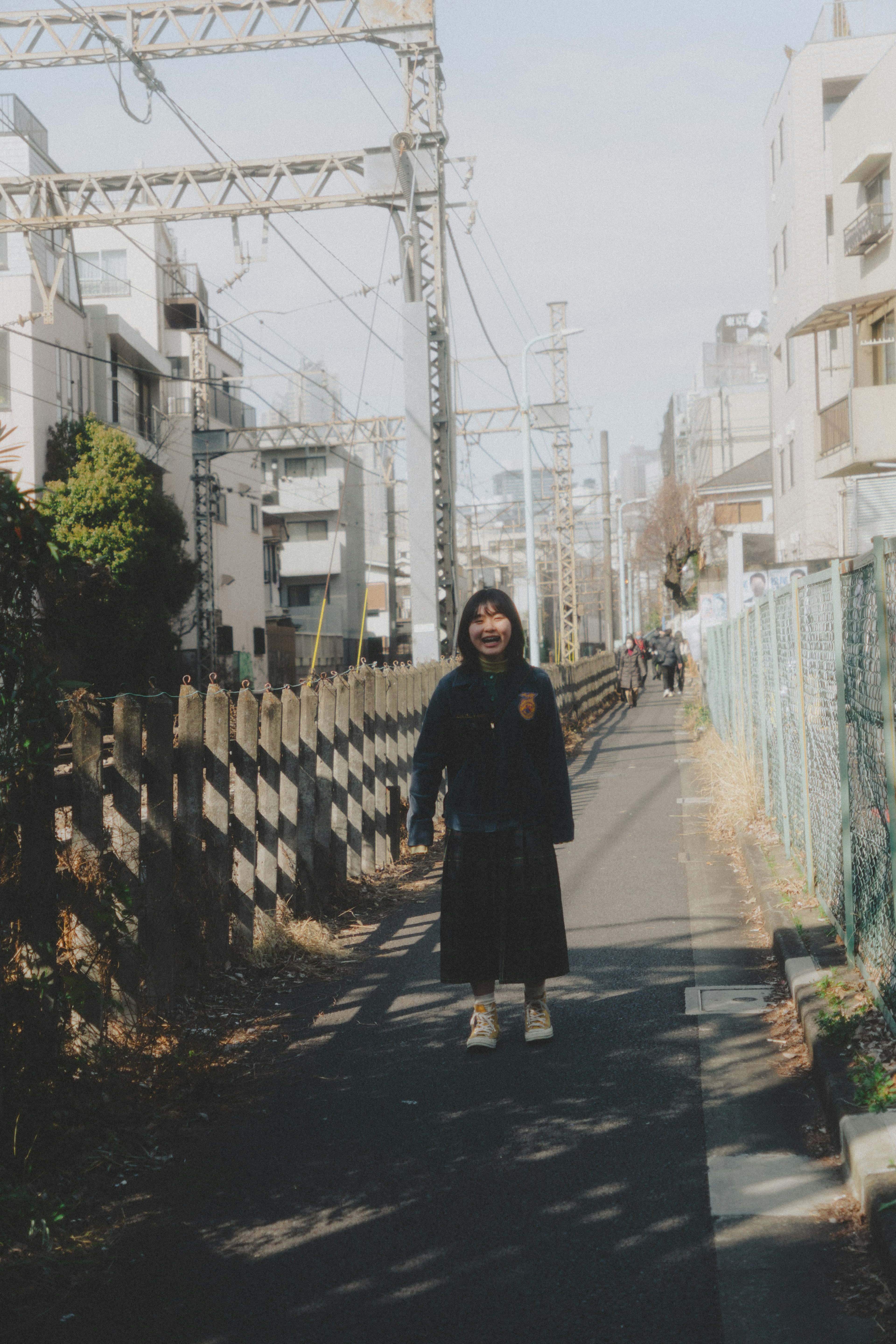 A young woman in black clothing standing on a street with buildings and trees