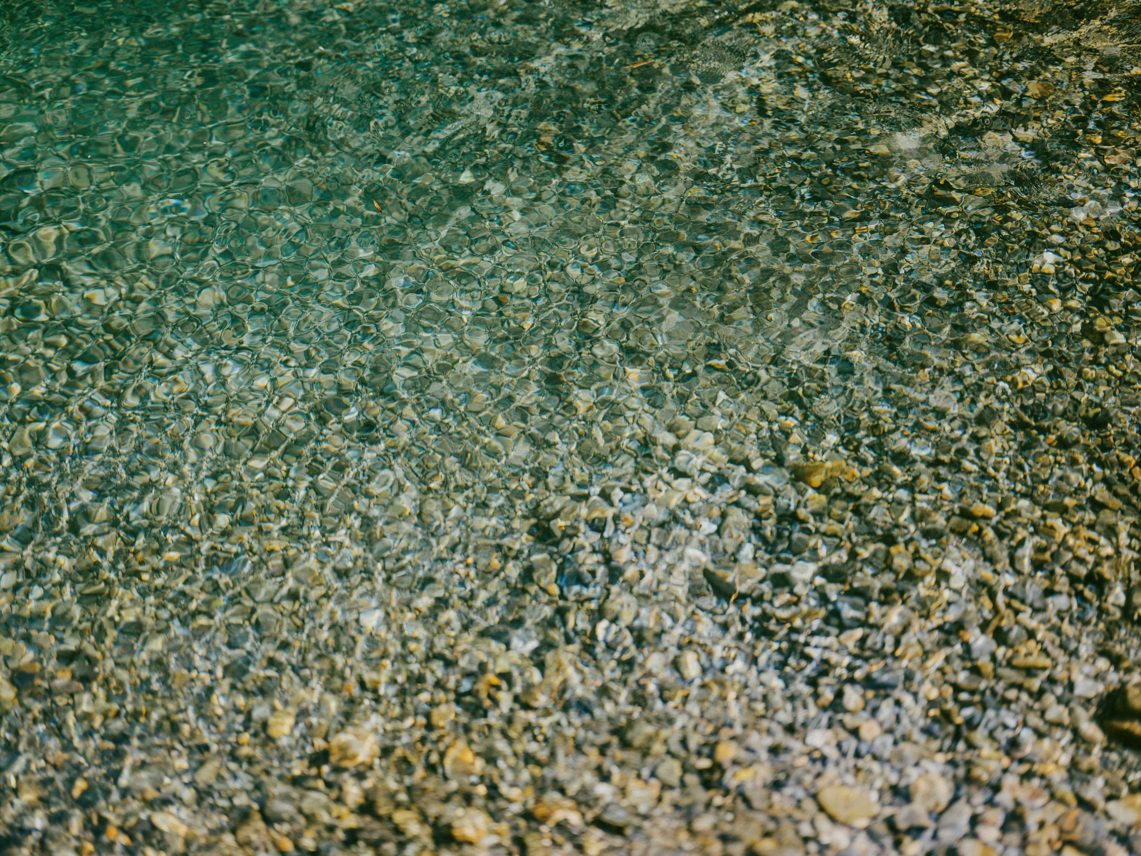 Klare Wasseroberfläche, die Kiesel und Sand darunter zeigt