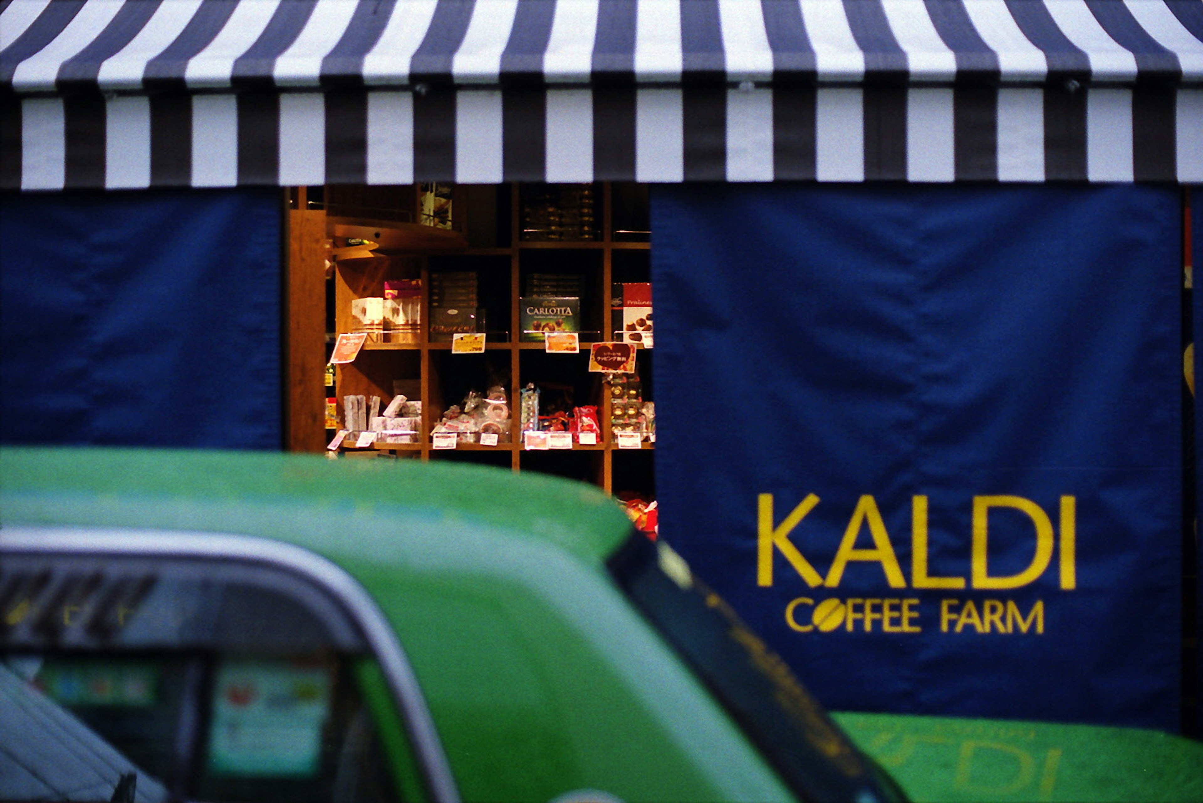 Café-Außenansicht mit blauen Vorhängen und einem gestreiften Vordach mit dem Namen KALDI COFFEE FARM