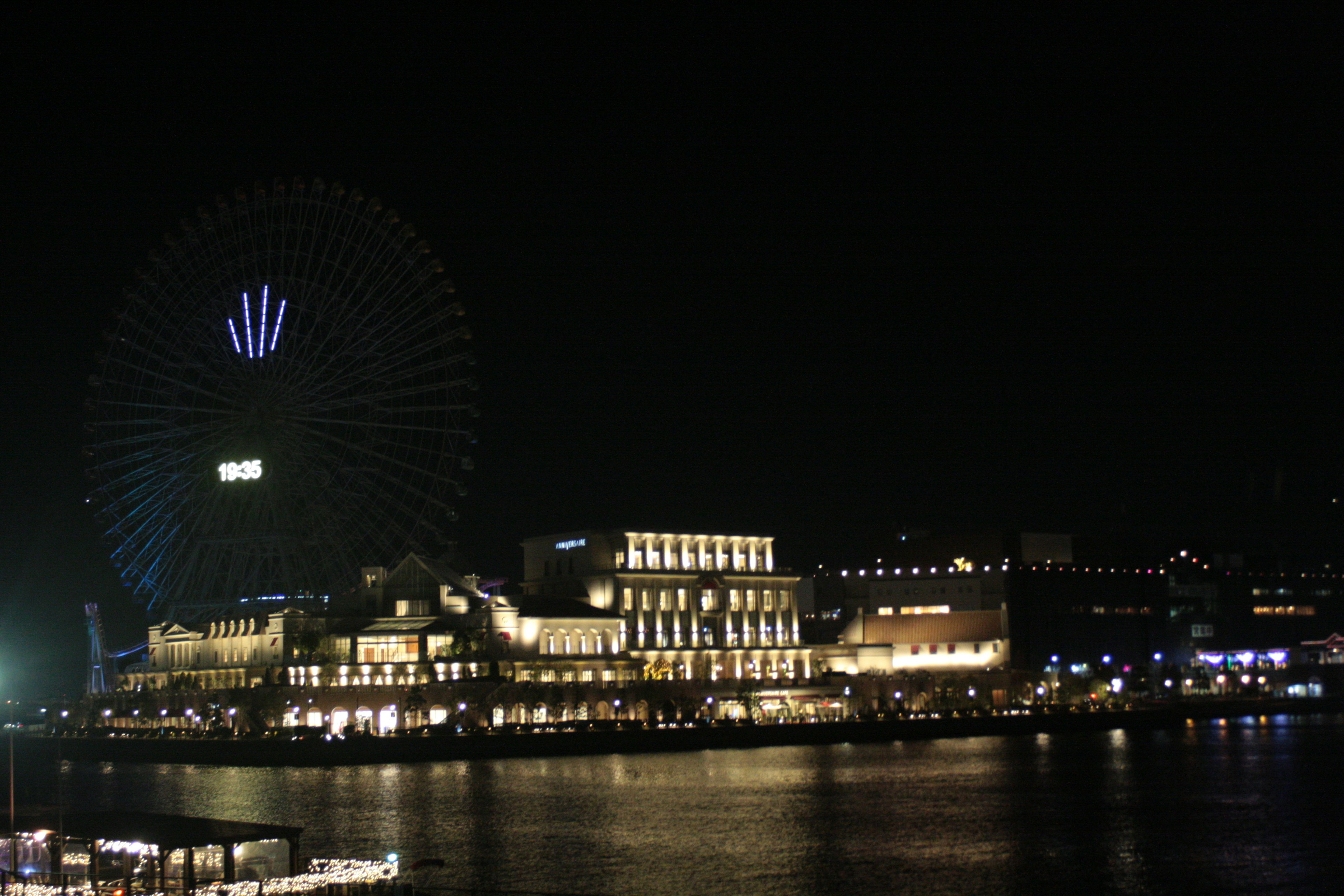 Illuminated buildings along the waterfront with a Ferris wheel at night