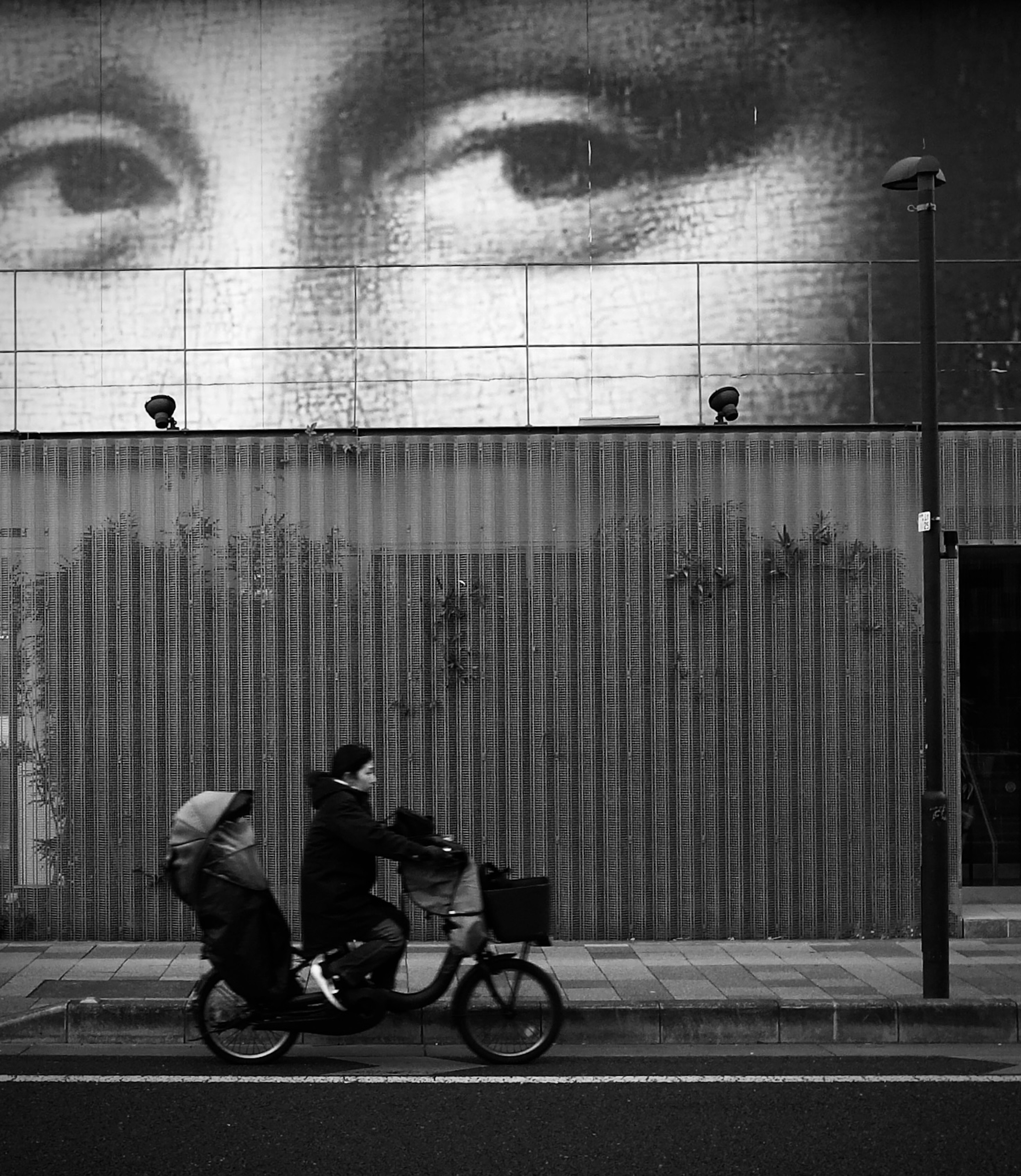 A person riding a bicycle in a black and white street with a large eye mural